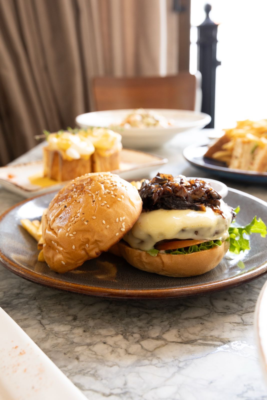 Gourmet burger with melted cheese and caramelized onions on sesame bun, served on ceramic plate at restaurant table.