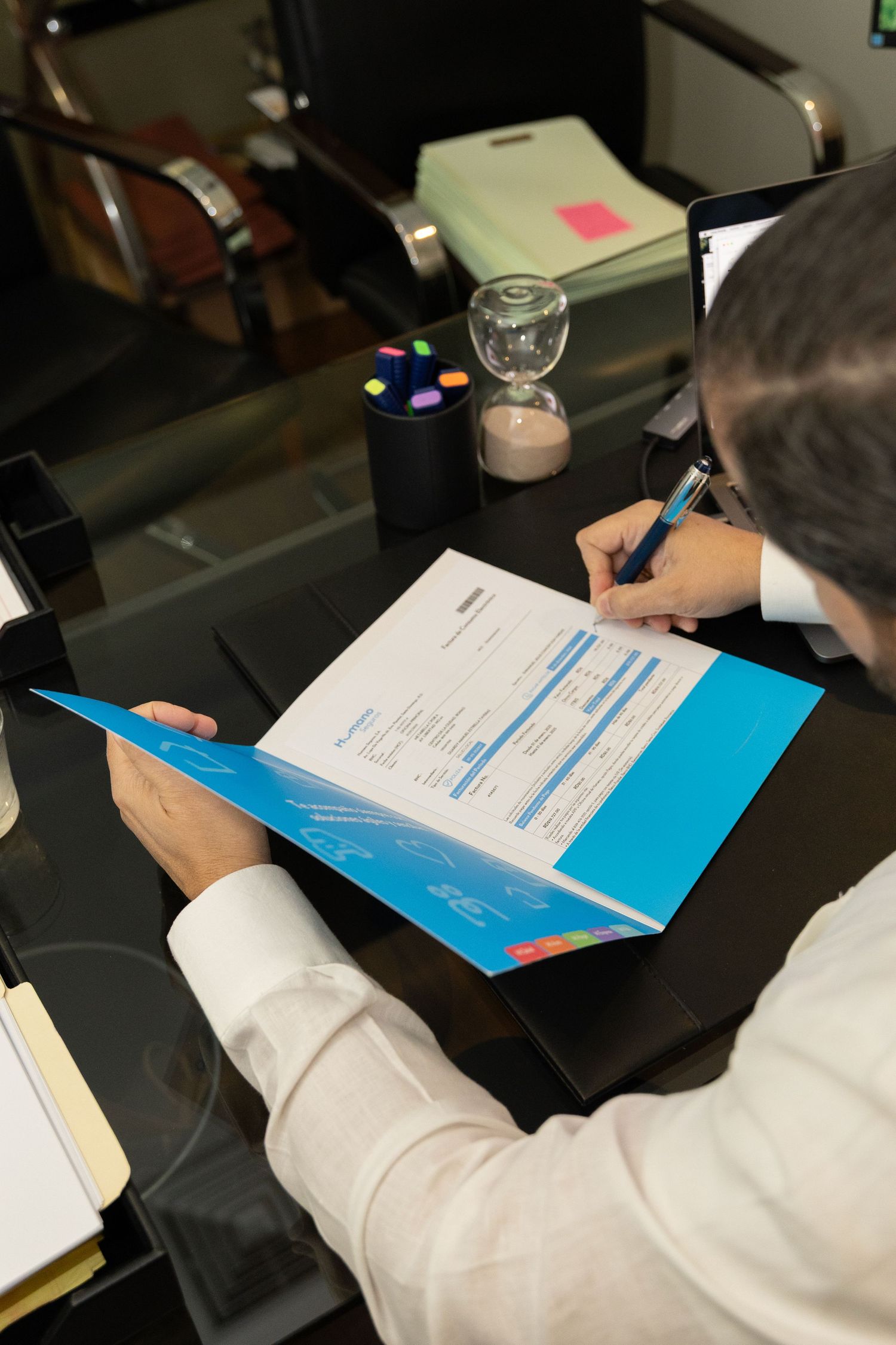 Business professional signing documents in a blue folder at a modern office desk with stationery.