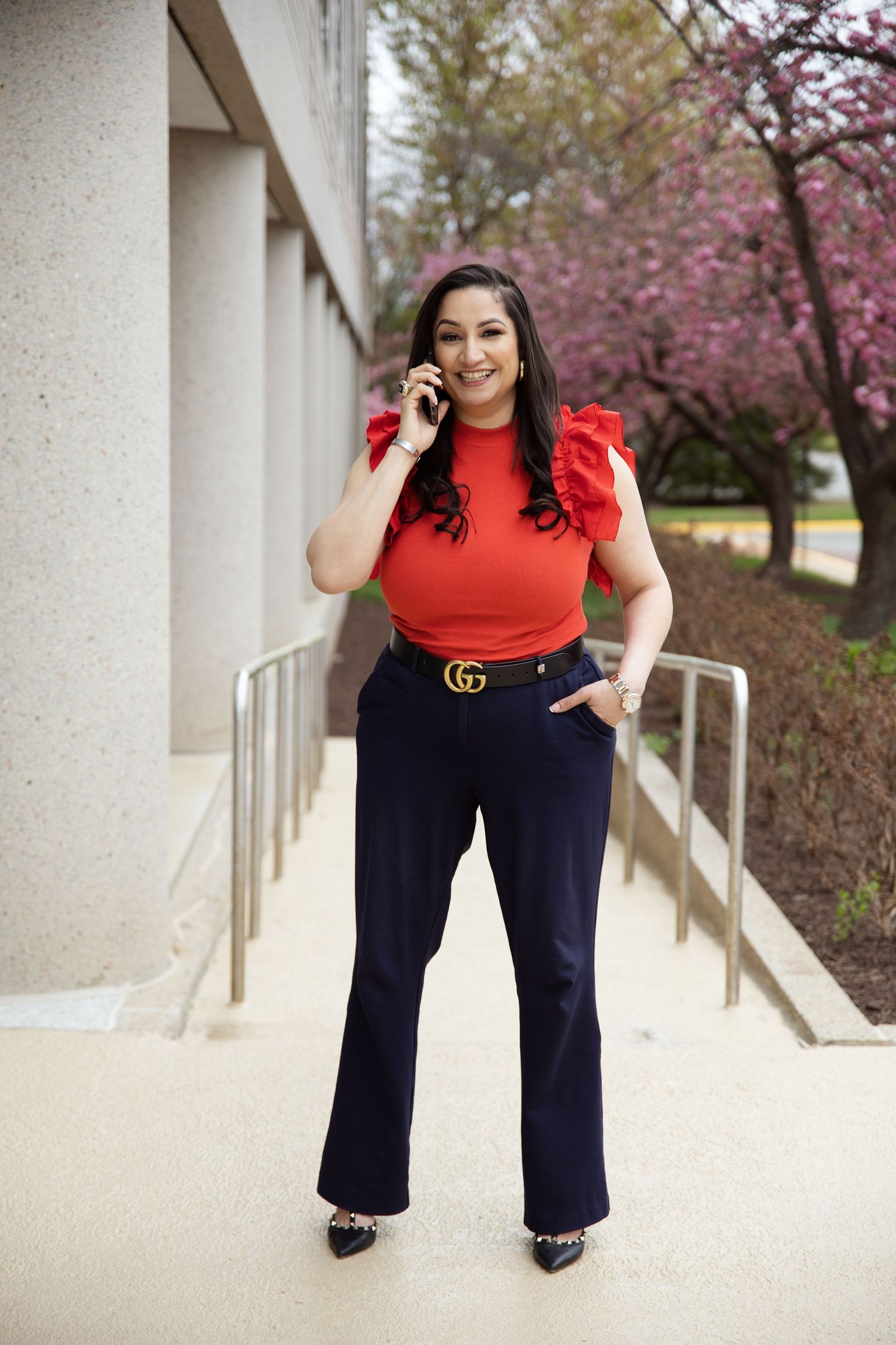 Stylish outfit featuring red top, navy pants and designer belt against cherry blossom background.