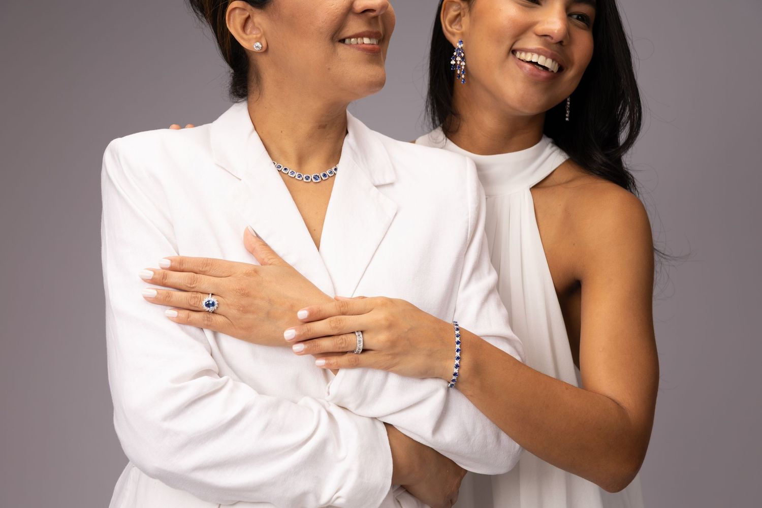 Two women in white outfits model elegant diamond jewelry including necklaces, rings, earrings, and bracelets.