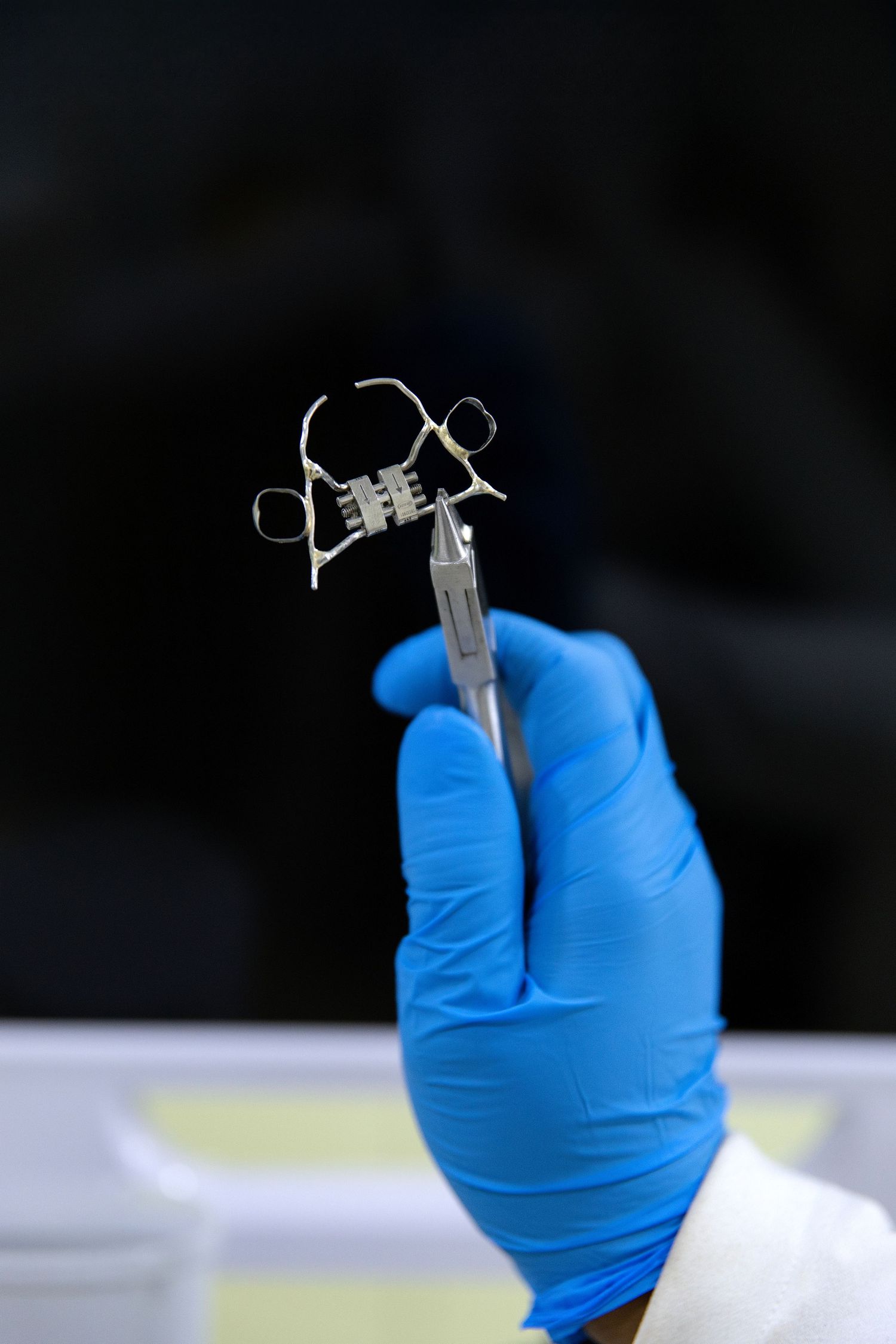 Gloved hand holding a small medical device with tweezers in a laboratory setting.