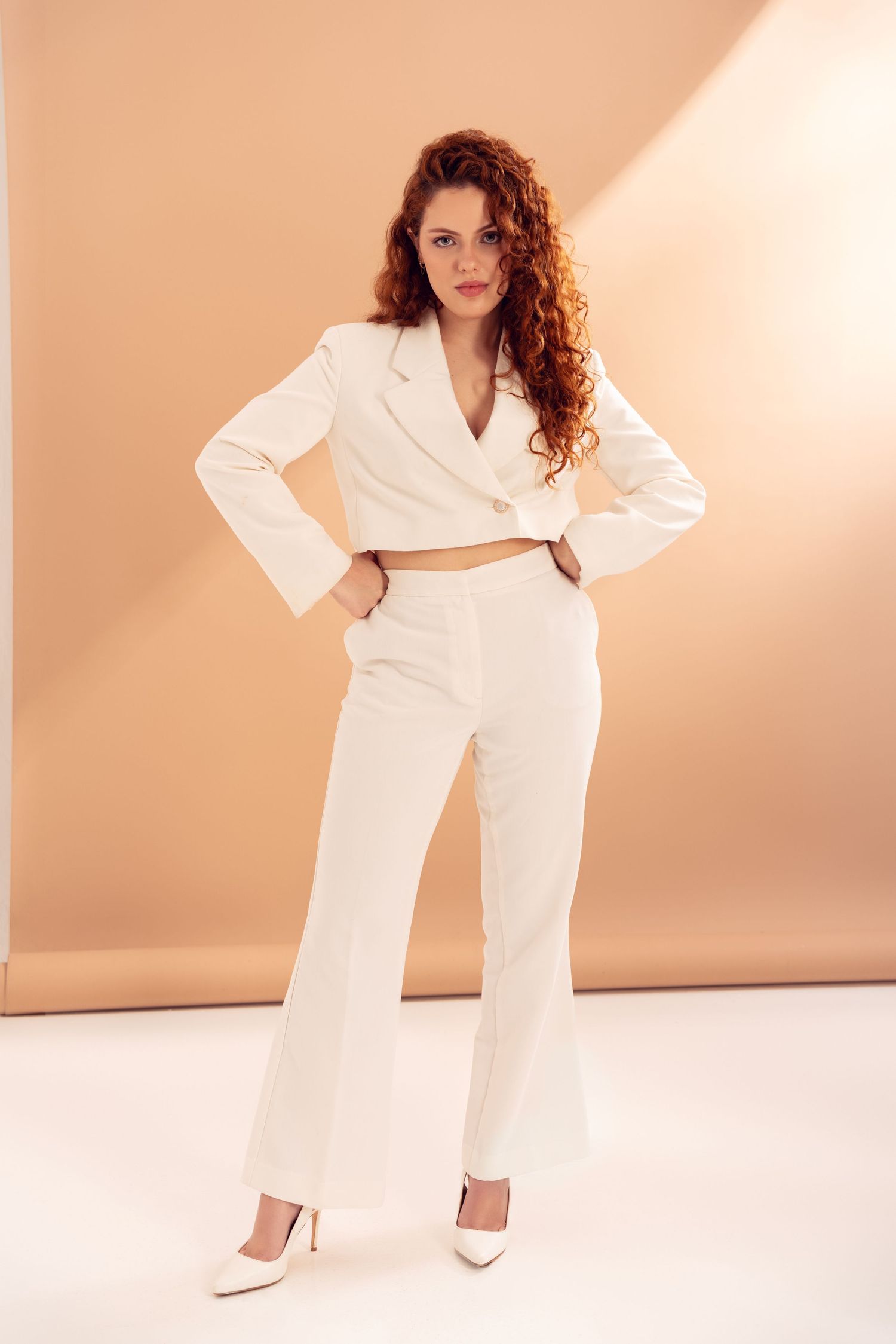 All-white ensemble with wide-leg pants photographed against peachy backdrop.
