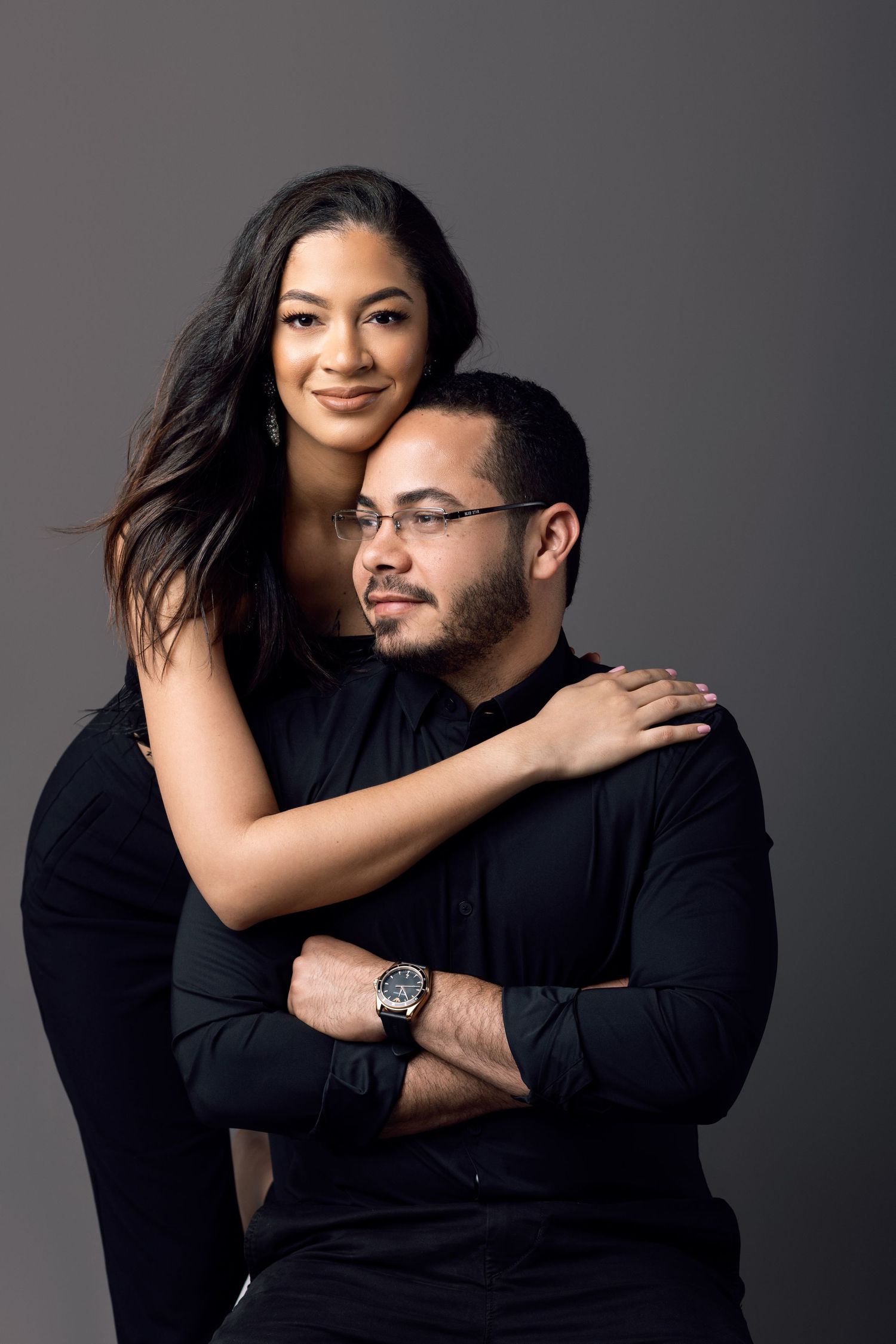 Intimate portrait of couple in black attire against dark studio background.