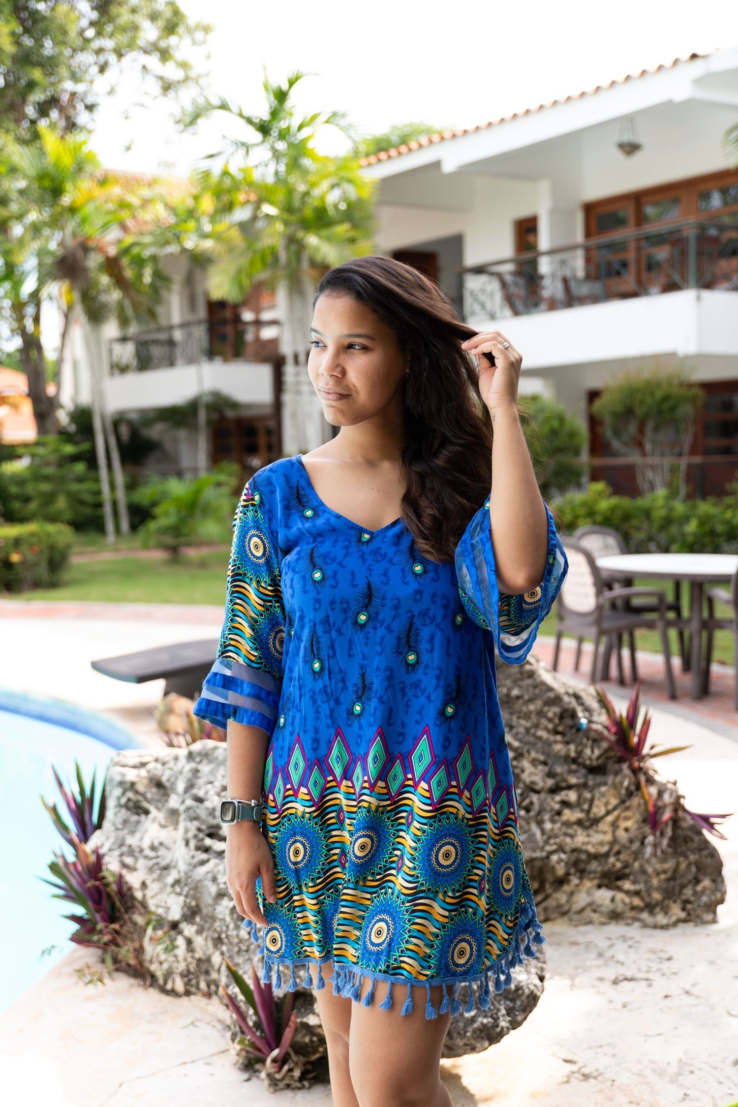 Woman in blue printed kaftan dress posing by a pool at a tropical resort.