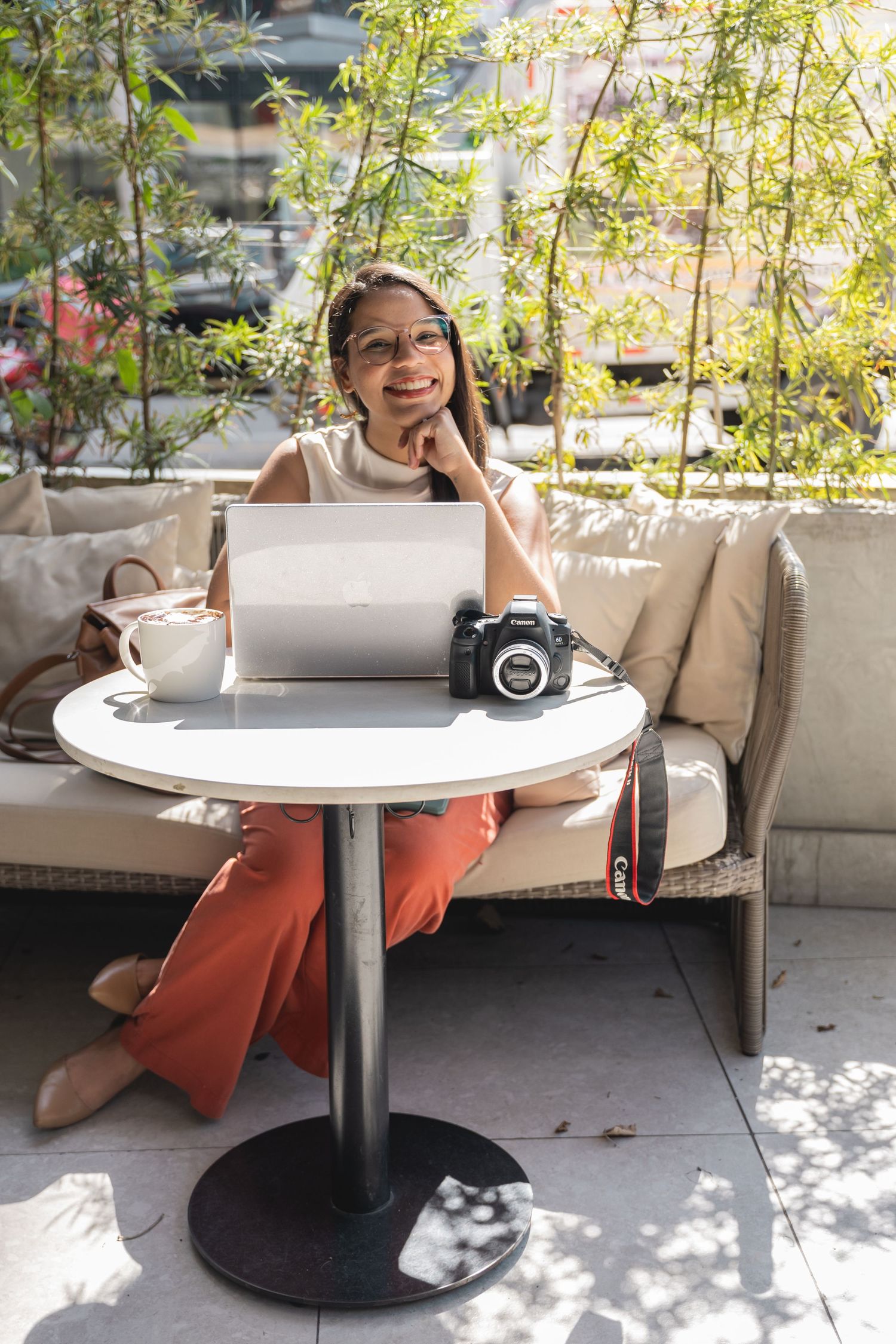 Woman working on laptop at outdoor cafe table with camera and coffee cup.