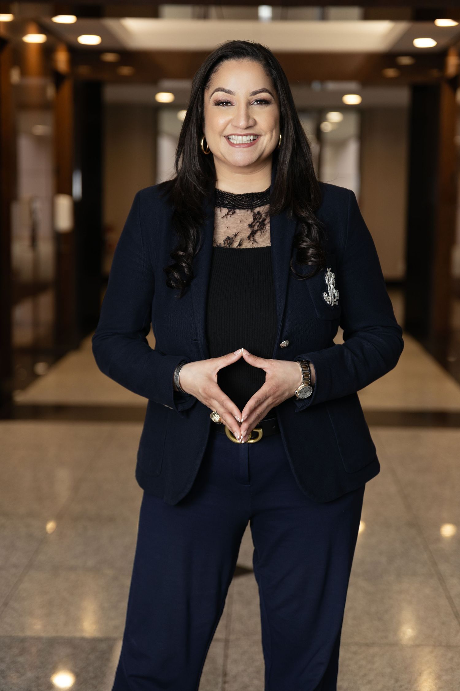 Business professional poses in navy blazer against modern indoor backdrop.