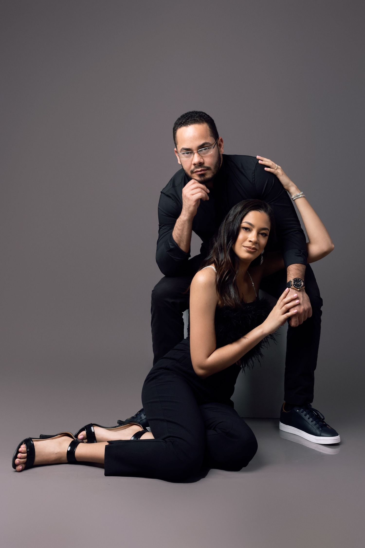 Stylish couple in black clothing posing together in studio setting.