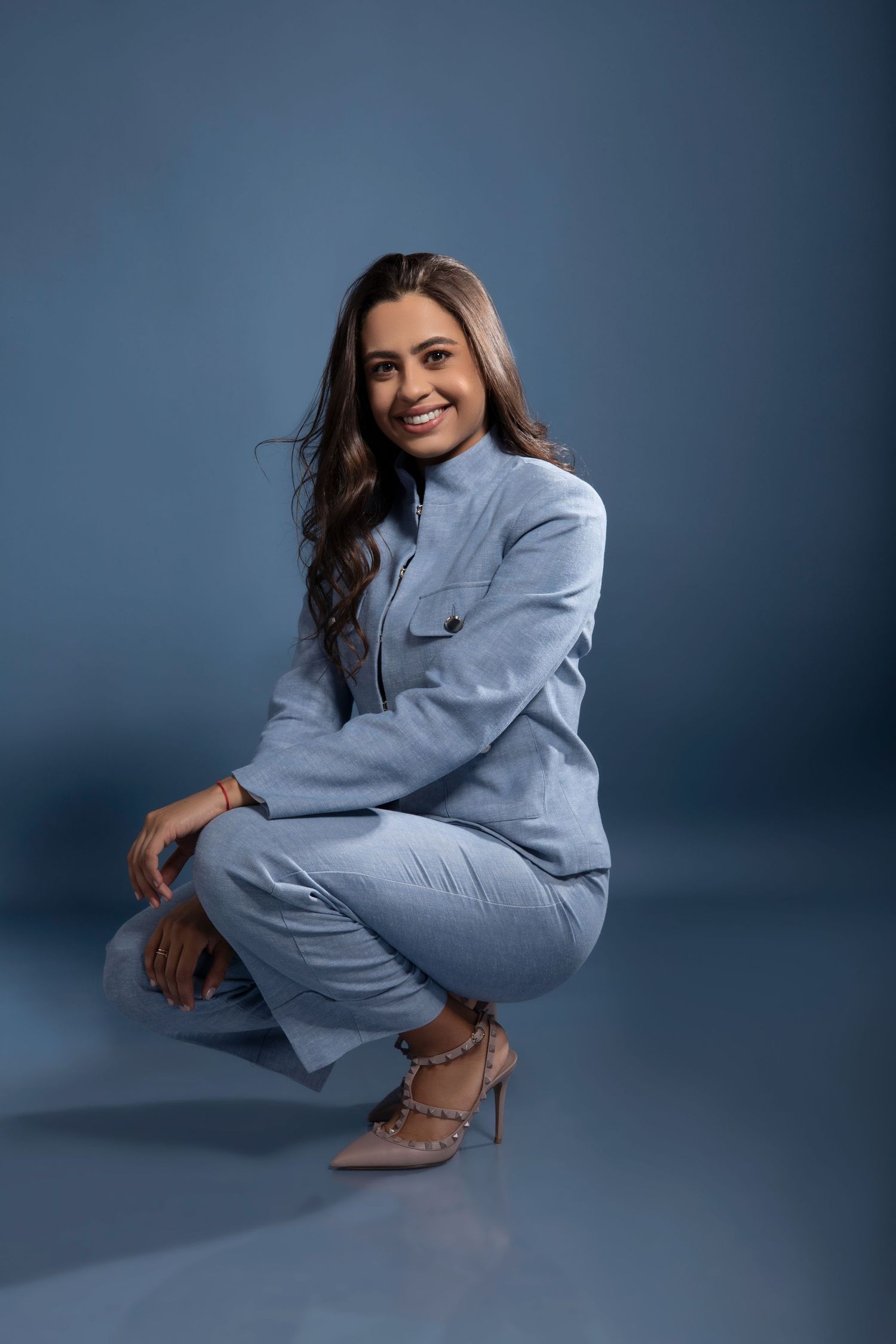 Professional portrait of person in light blue suit crouching against blue backdrop.