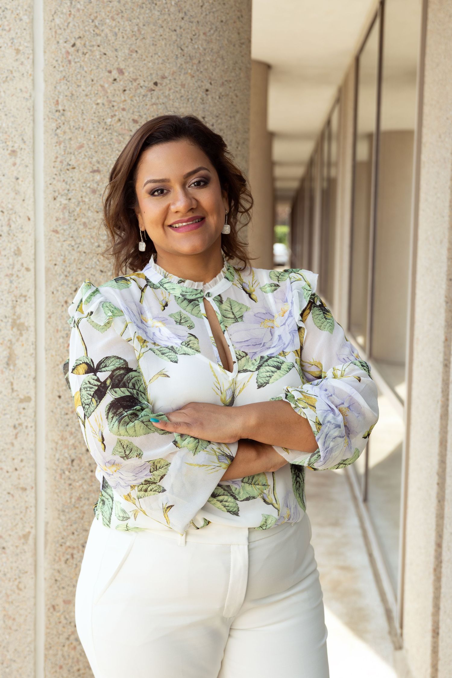 Spring fashion look with floral print blouse and white pants in architectural setting.