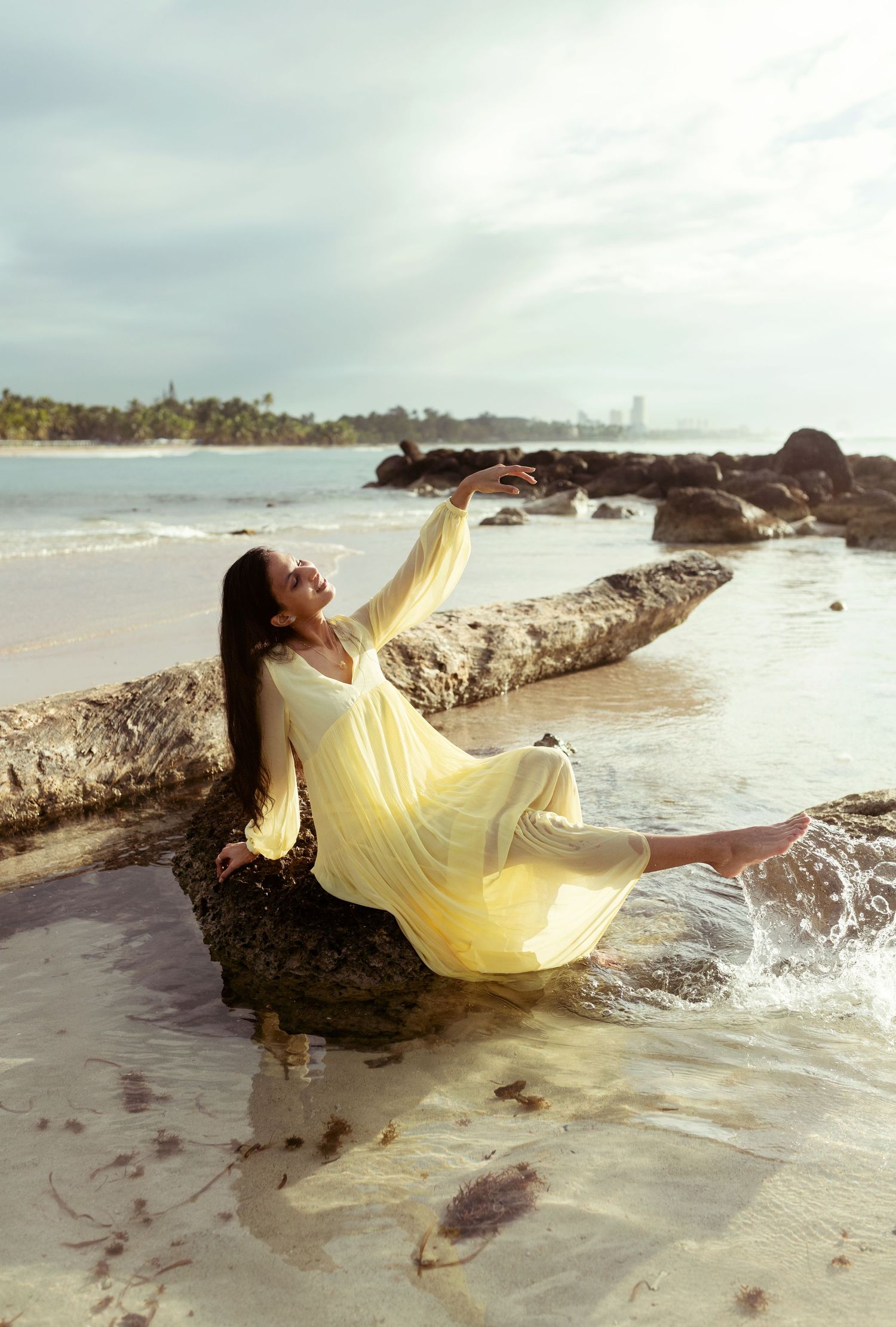 A flowing yellow dress creates dramatic movement against a rocky beach landscape.