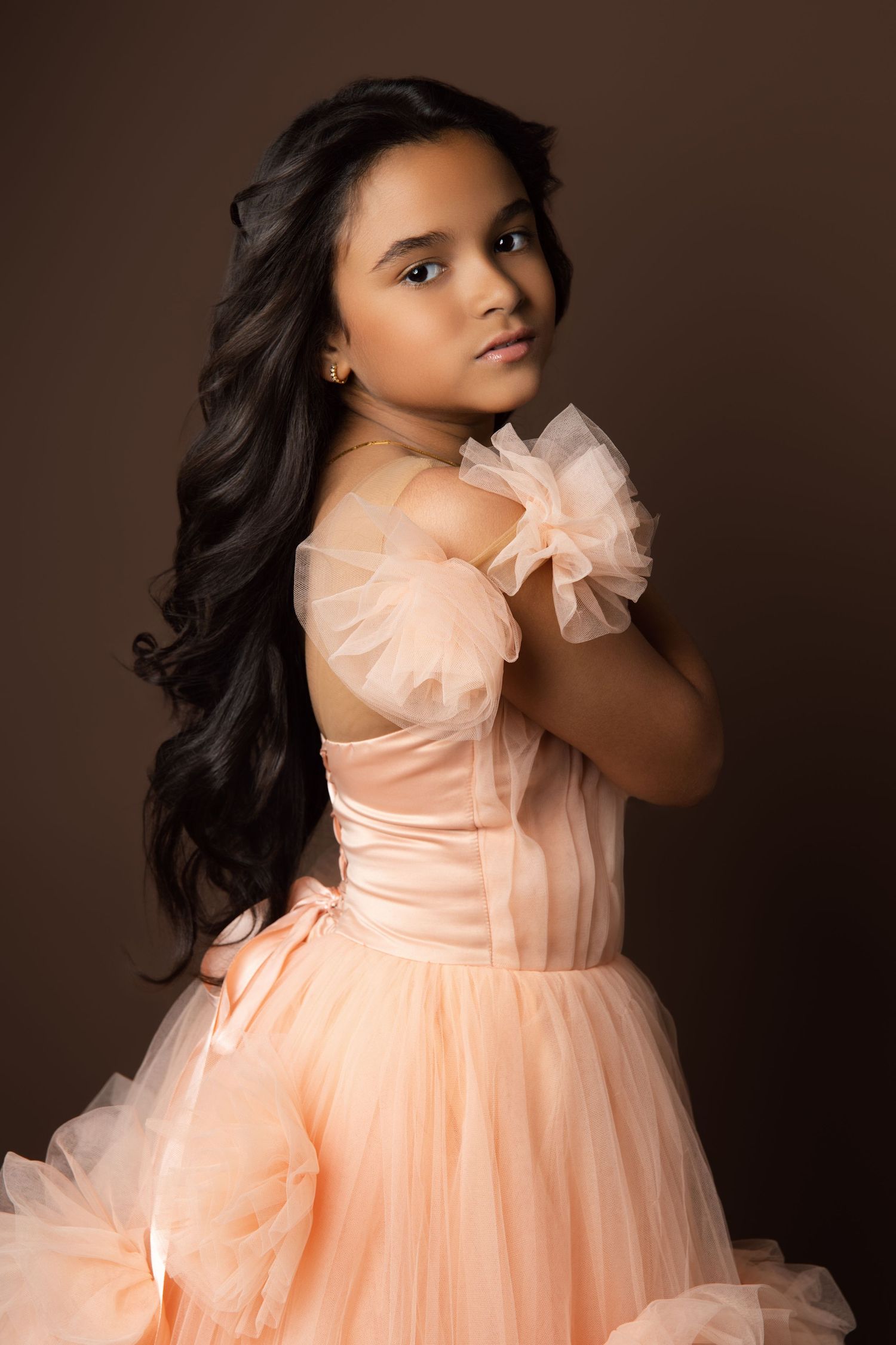 Dramatic studio portrait featuring peach colored formal gown against dark background.