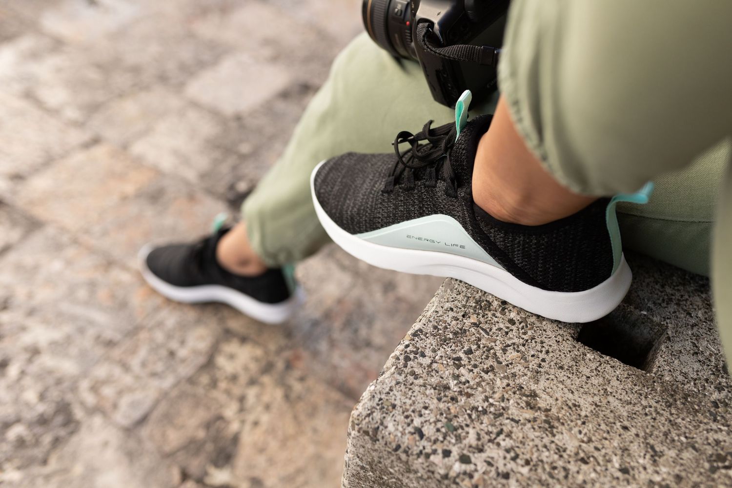 Person sitting on stone steps wearing black and mint athletic sneakers with white soles and green jogger pants.