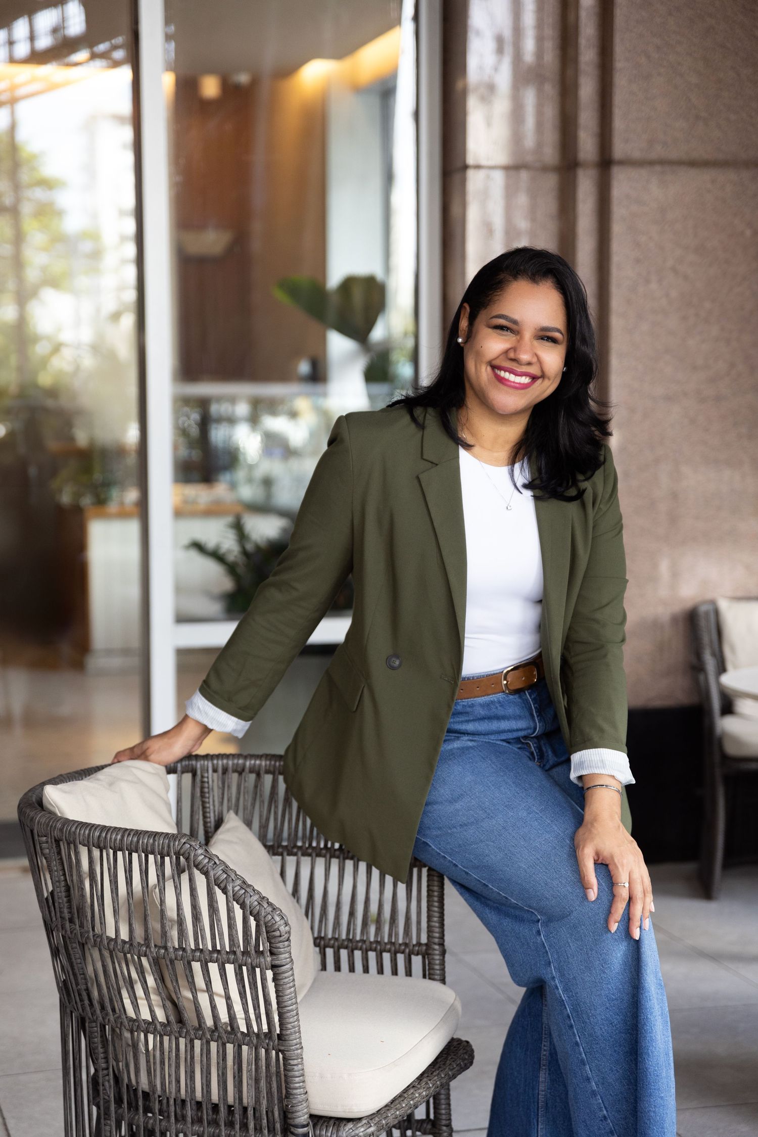 Casual business look featuring olive blazer, white top and jeans on outdoor patio.