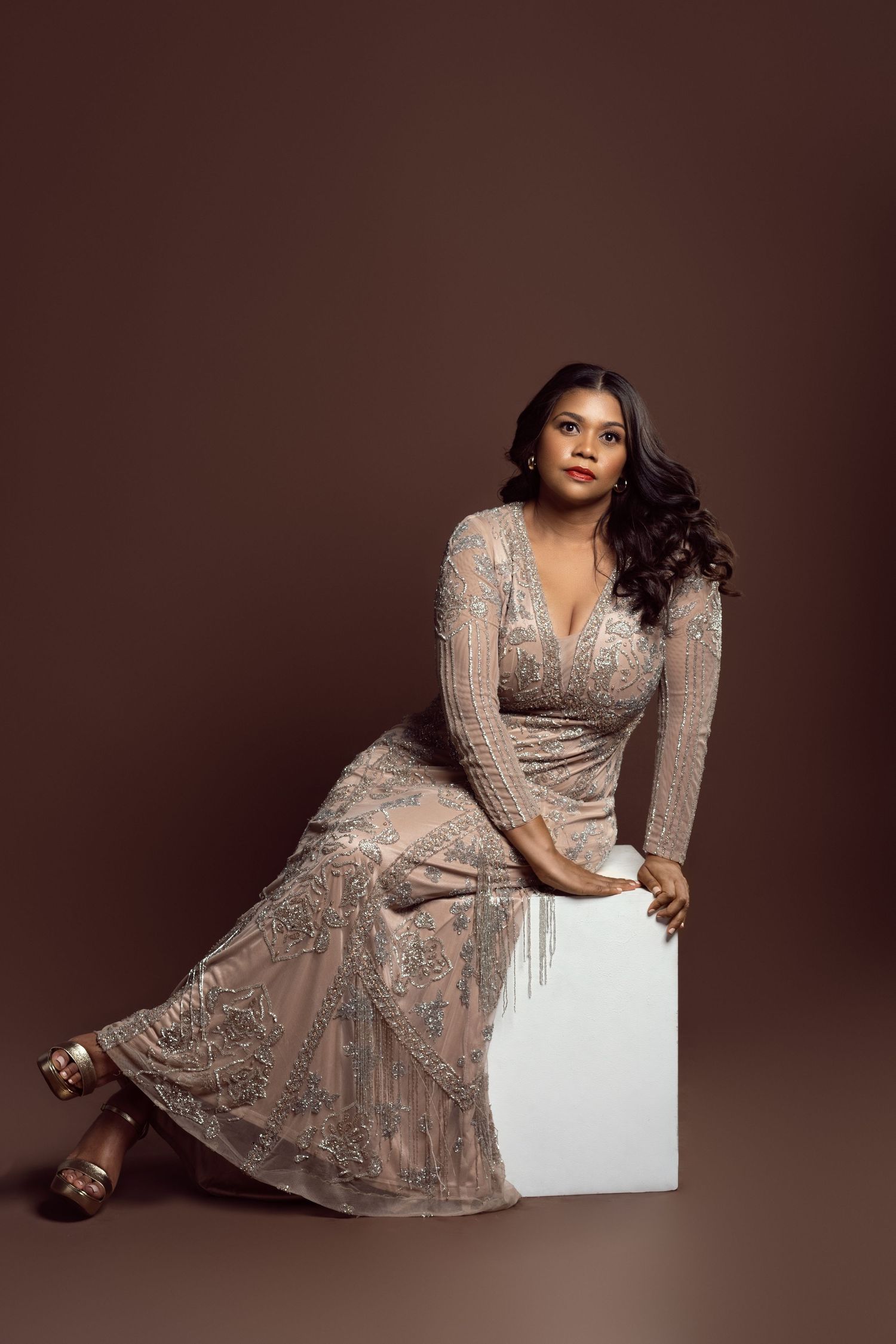 Elegant poses in sparkly beige evening gown against dark backdrop.