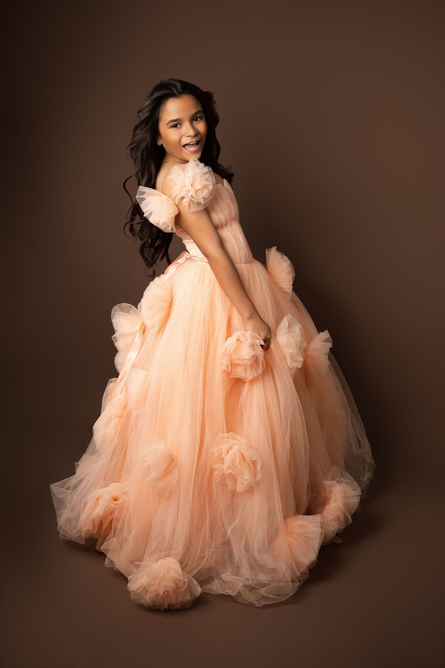 Flowing peach tulle dress photographed in elegant studio portrait setting.