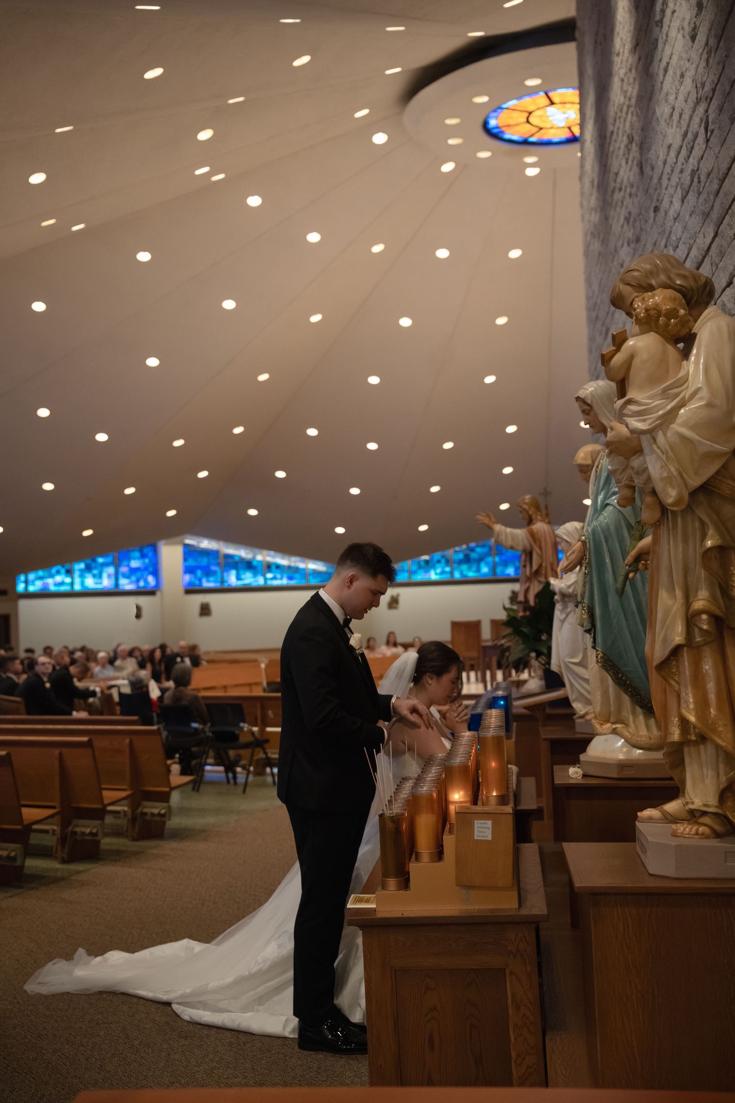 Church interior with spotlit ceiling and religious statues during wedding ceremony.