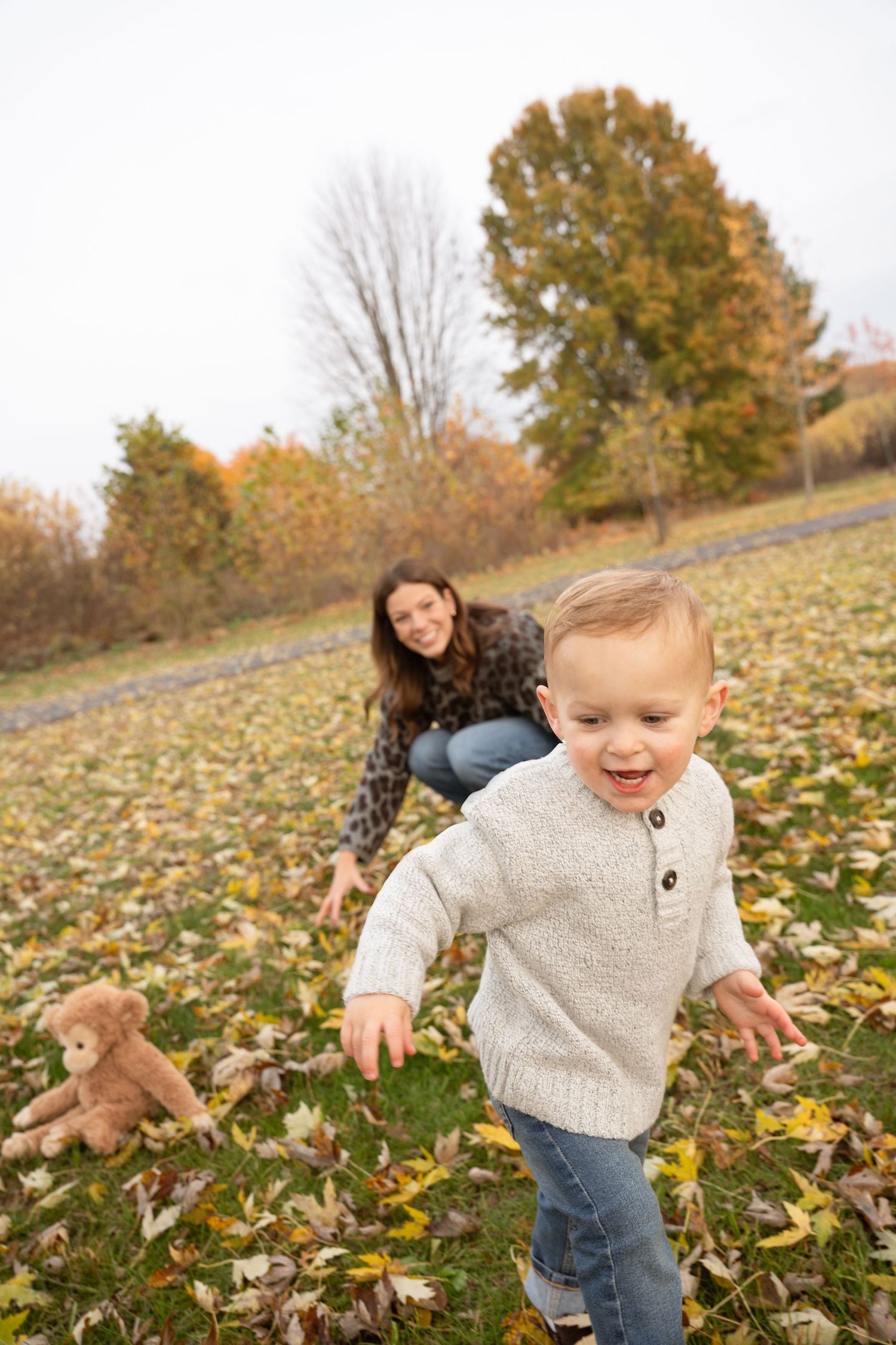 Little one runs joyfully through fallen autumn leaves on grass during outdoor photo session.