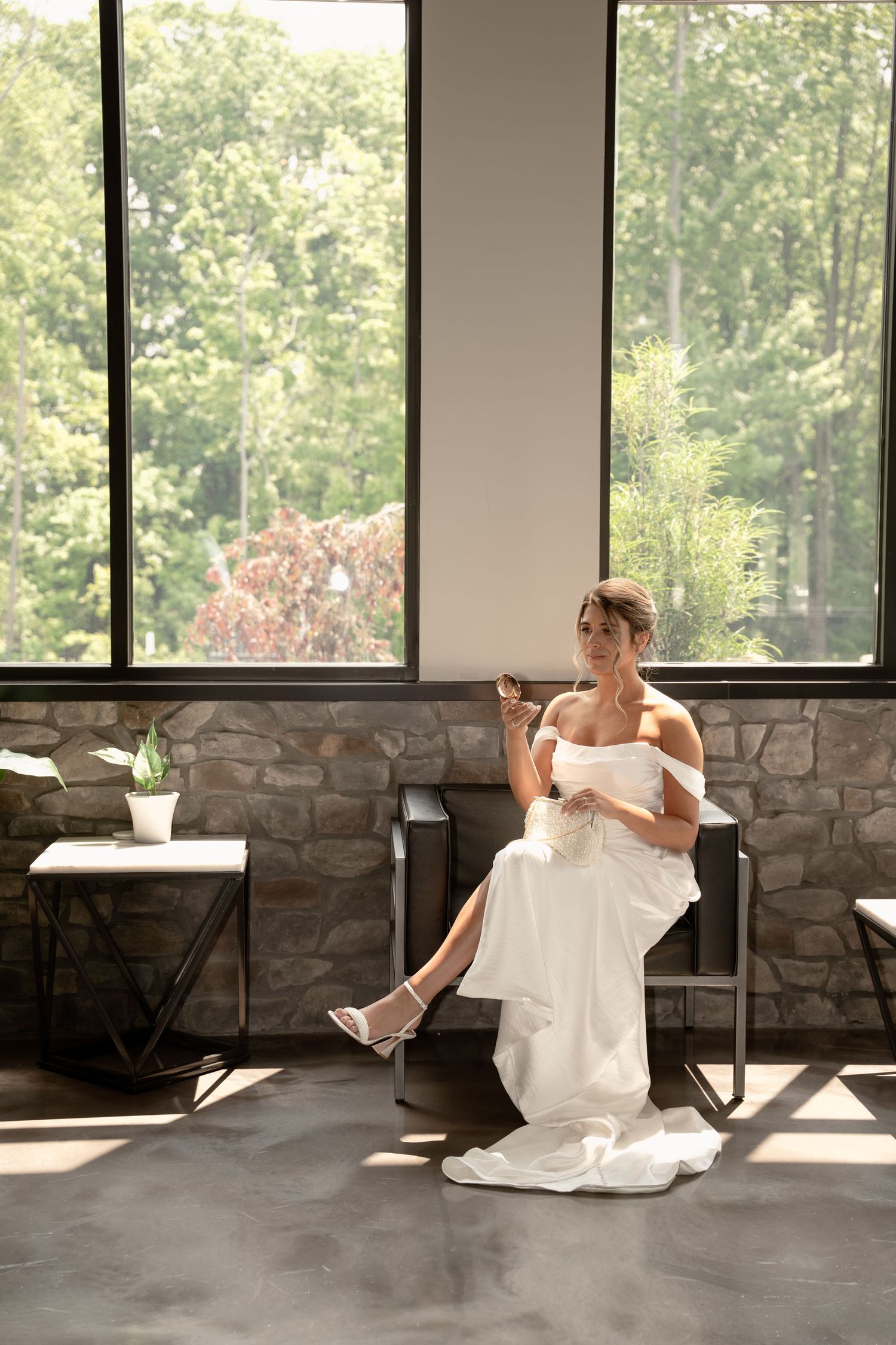 Bride in flowing white dress poses playfully in modern room with large windows.