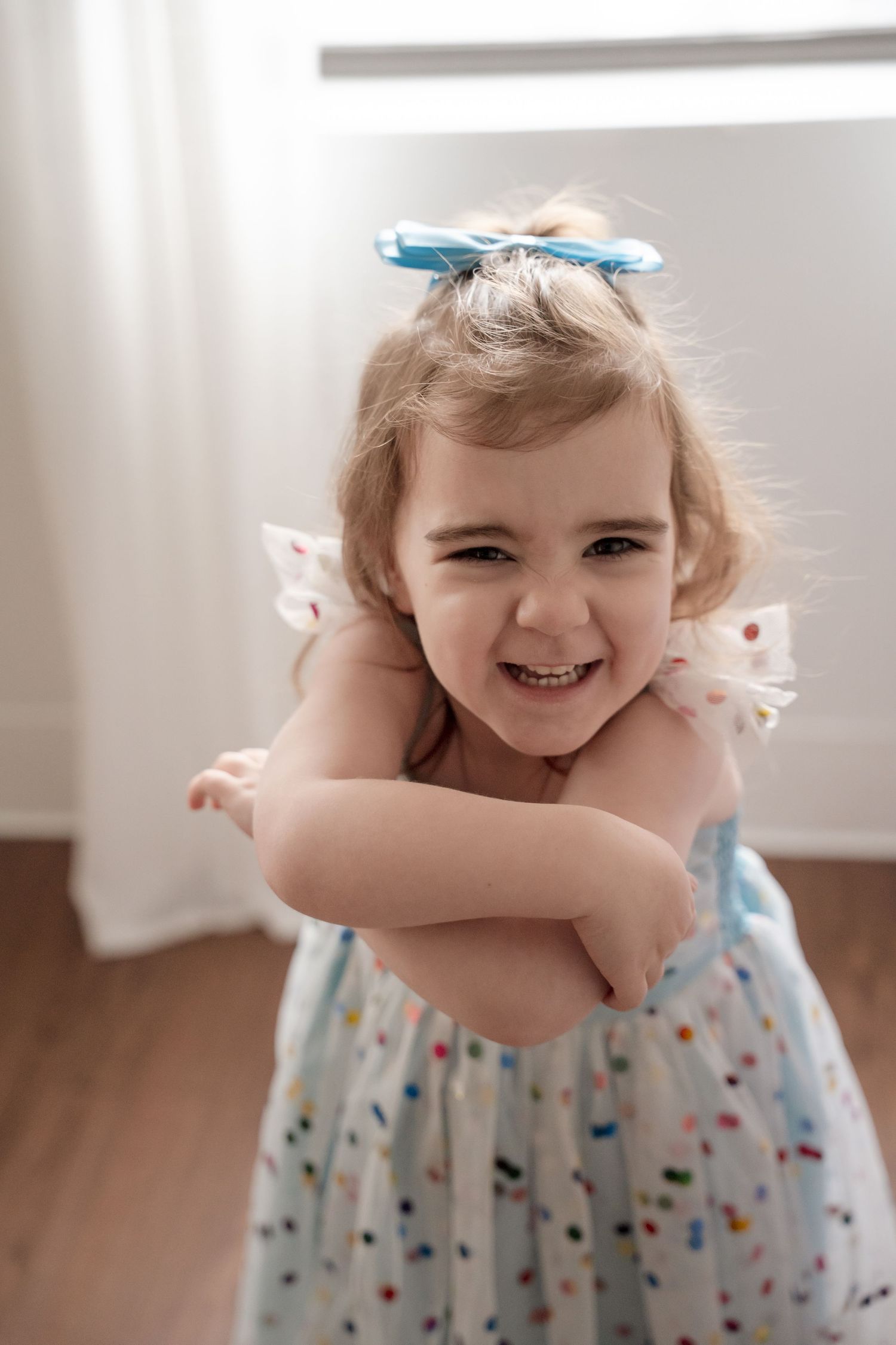 Young child in polka dot dress giggling and hugging herself with joy.