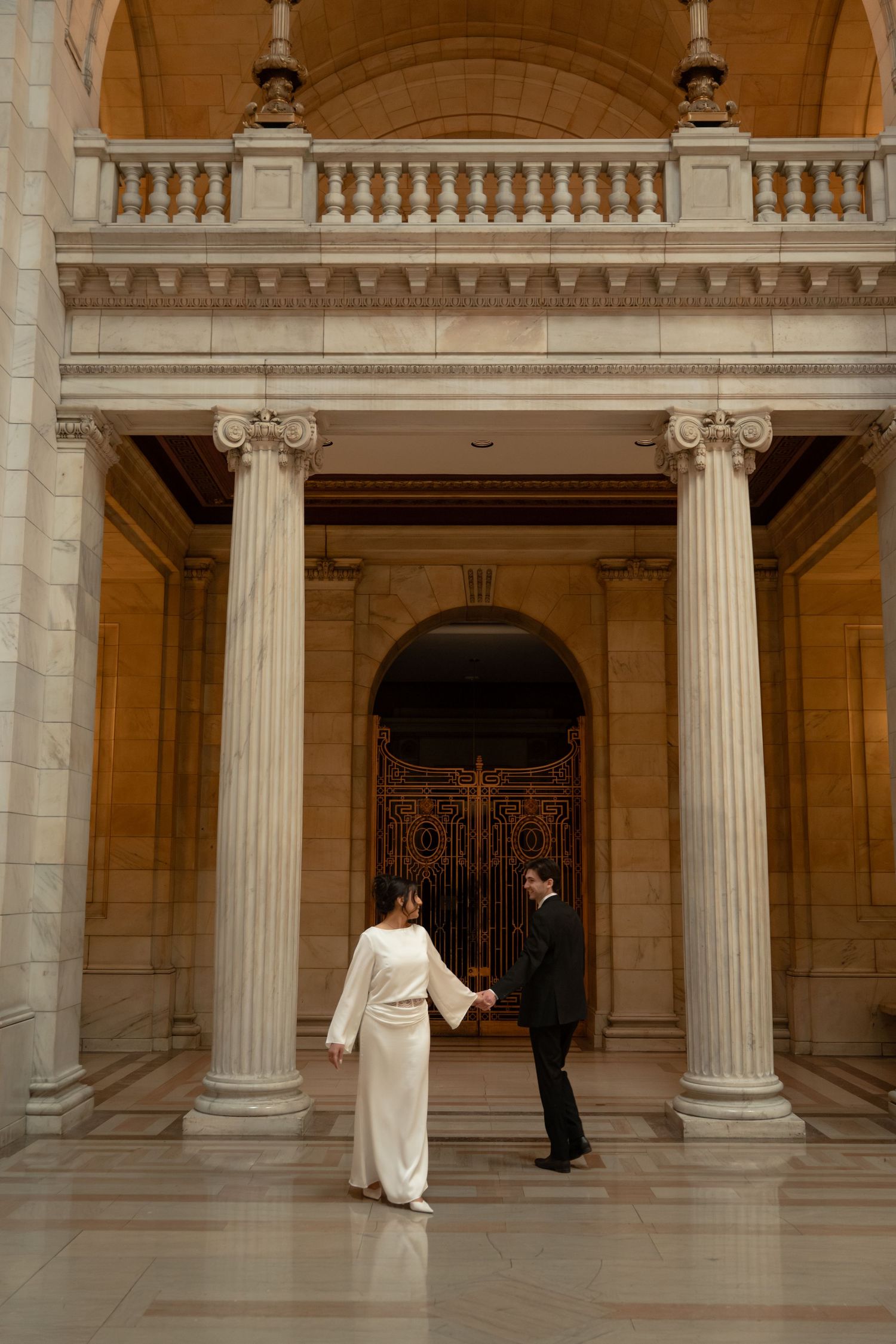 Elegant architectural setting with classical columns and arches creating dramatic framing for couple.