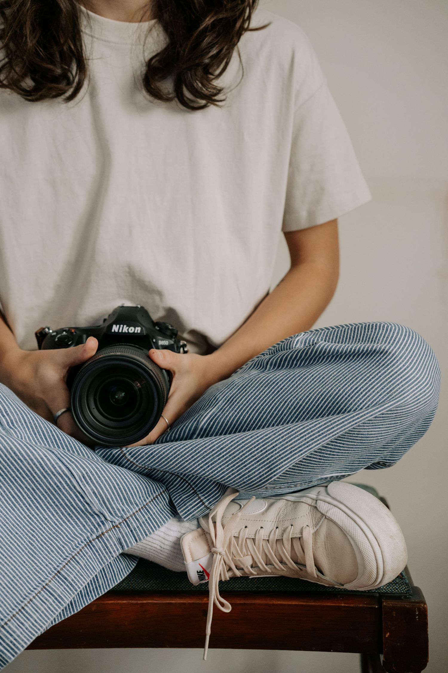 Alexa P. Artistry in casual attire holding camera while sitting cross-legged.