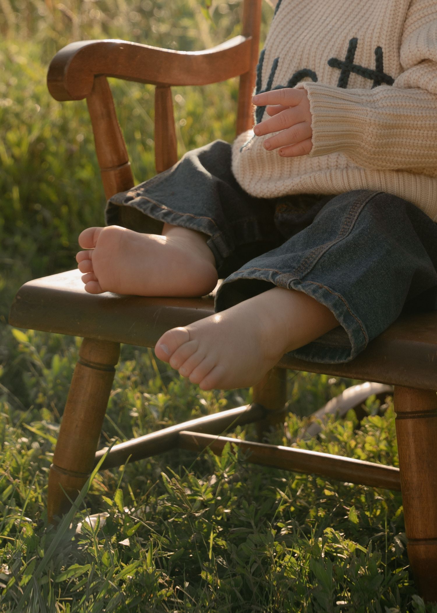 Close-up of little one resting on wooden chair in sunlit grass.