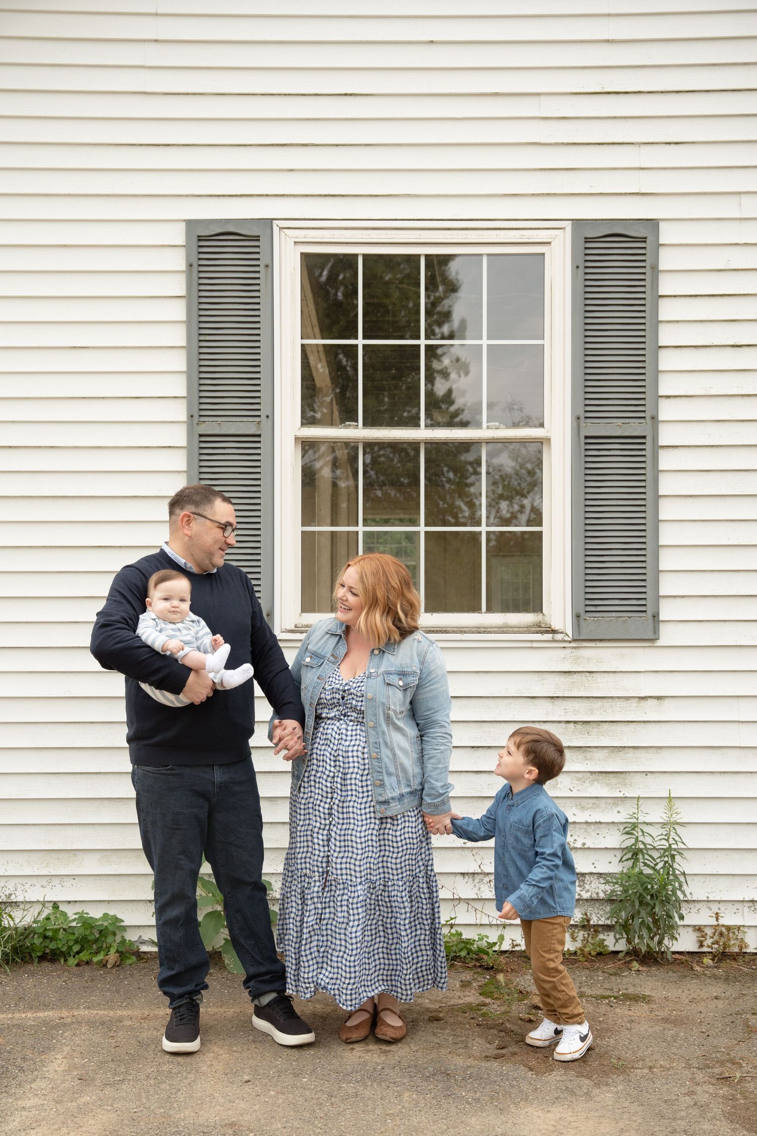 Family group poses casually against white siding of house with gray shuttered windows.