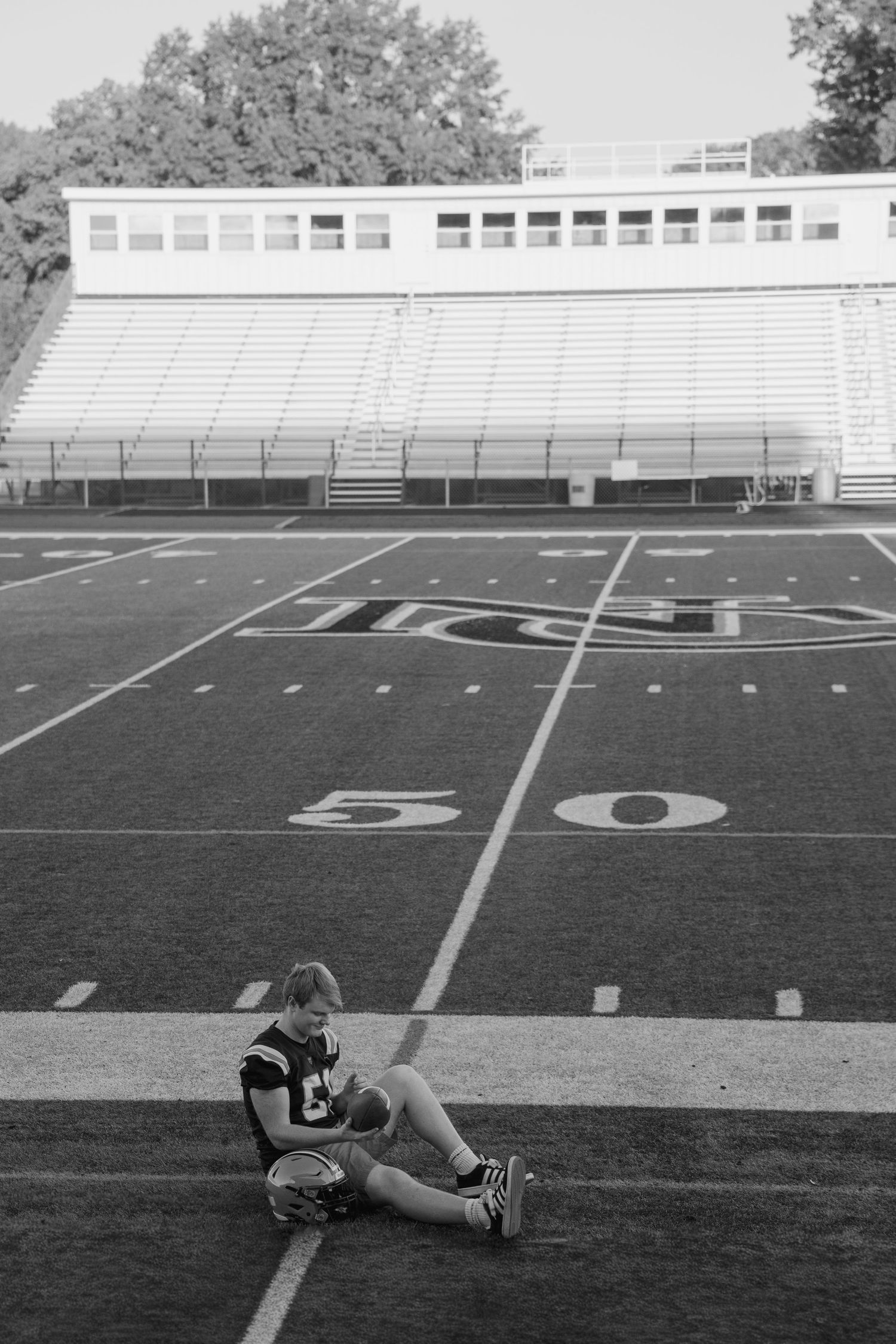 Empty football field with yard lines and bleachers in black and white senior session photography.
