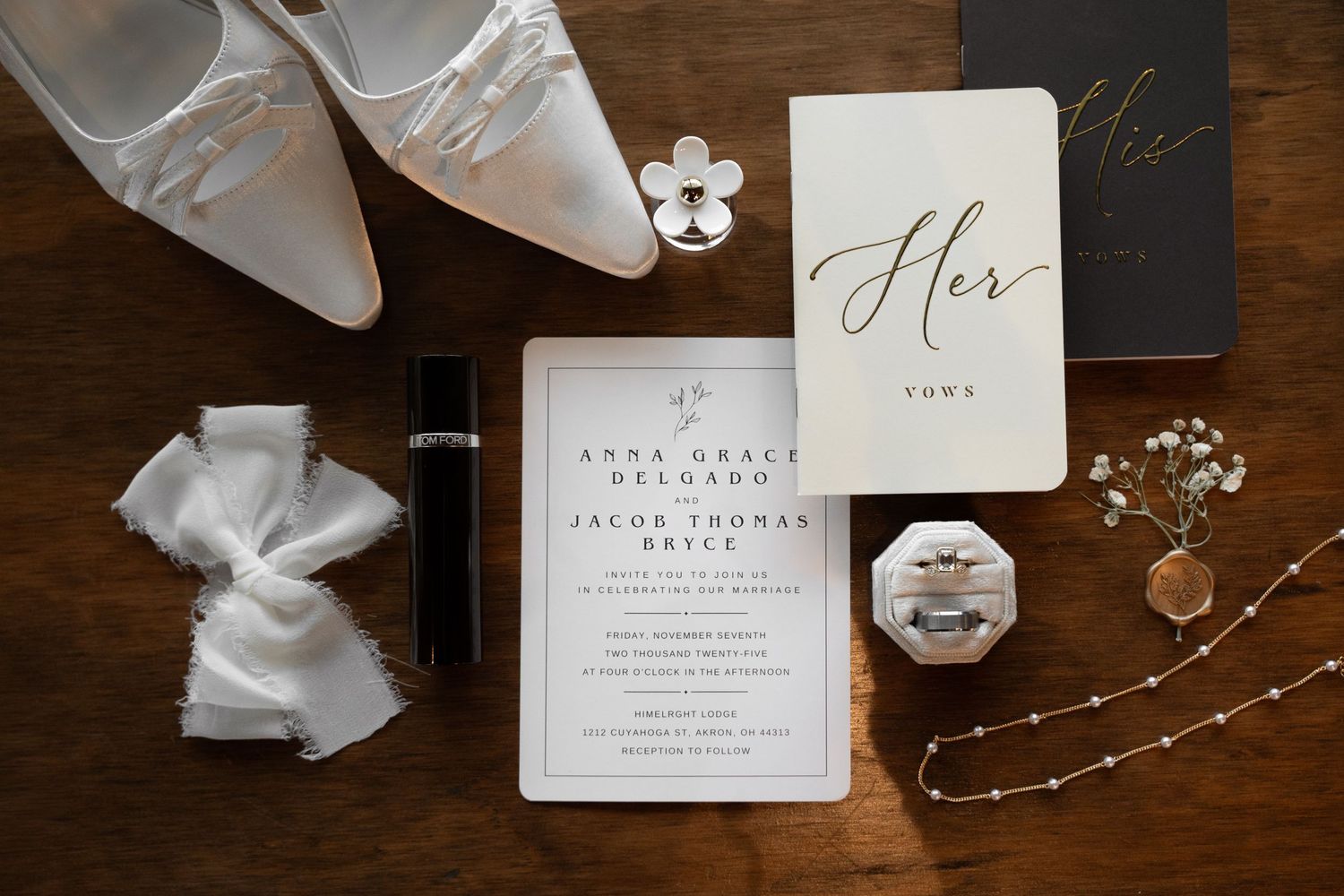 Wedding details including invitations, jewelry and accessories arranged on dark wood surface.