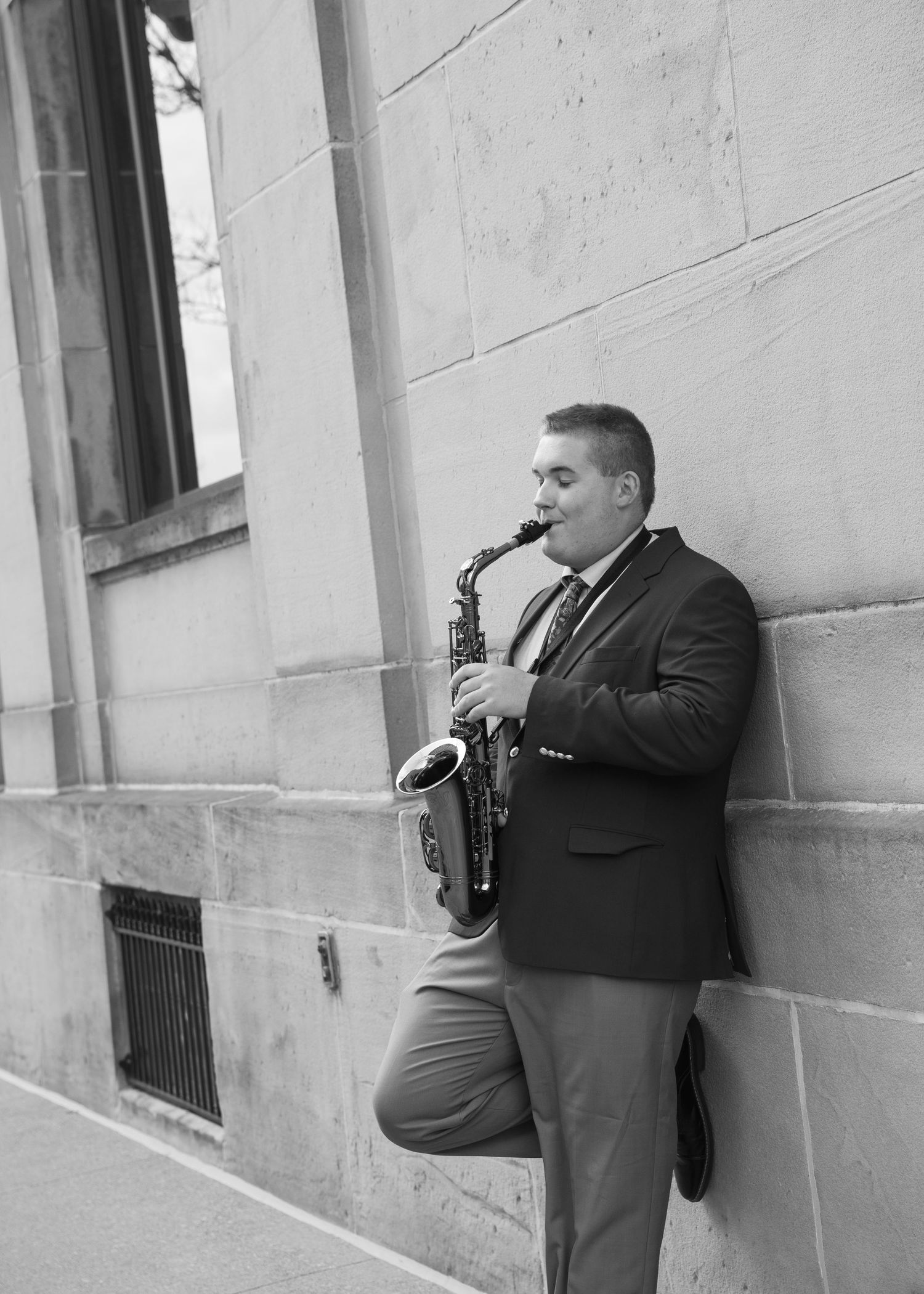 Black and white senior portrait of saxophone player performing against architectural backdrop.