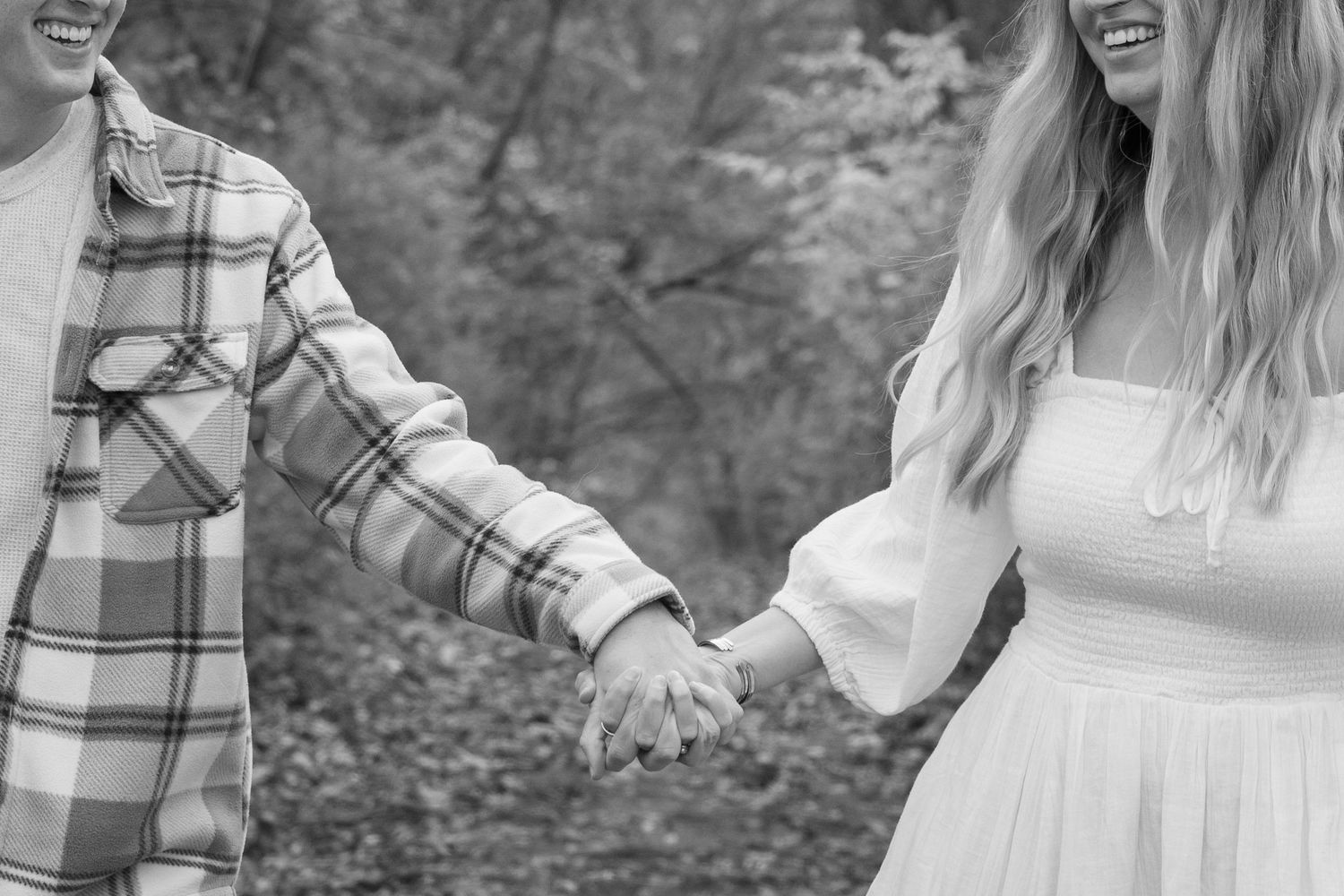 Couple walking through a wooded area hand in hand in black and white.