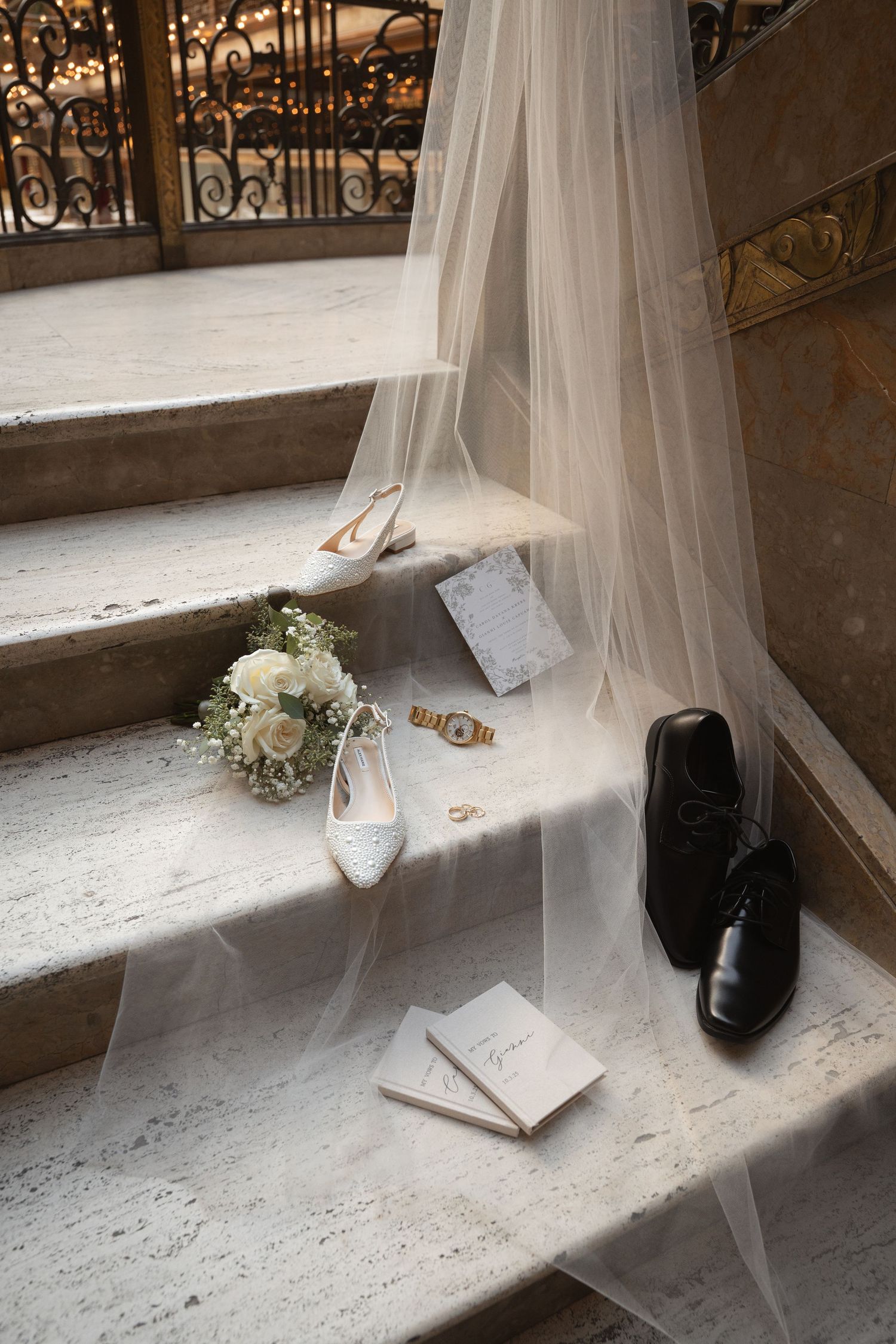 Wedding accessories including rings, shoes, veil and invitation card arranged on a stone windowsill in natural light.