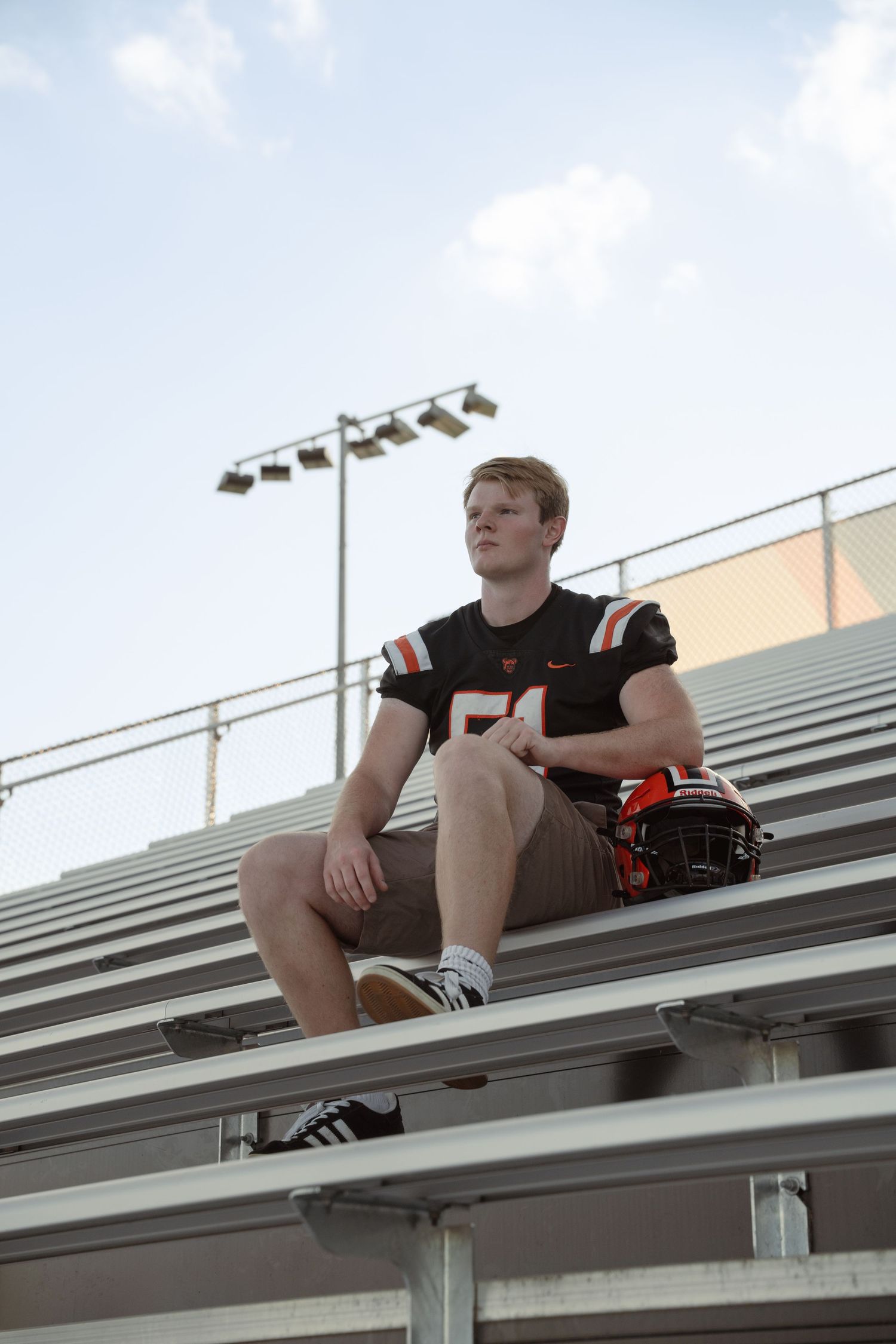 A senior in football gear sitting on metal bleachers looking into the distance.