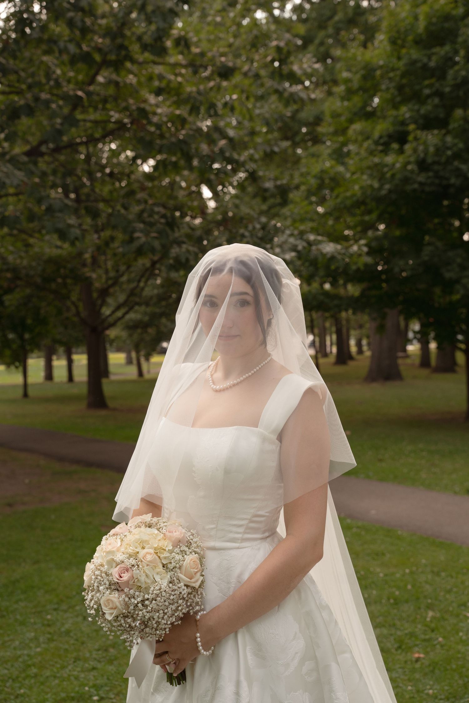 Bride in white dress holds delicate bouquet of baby's breath while walking through park.