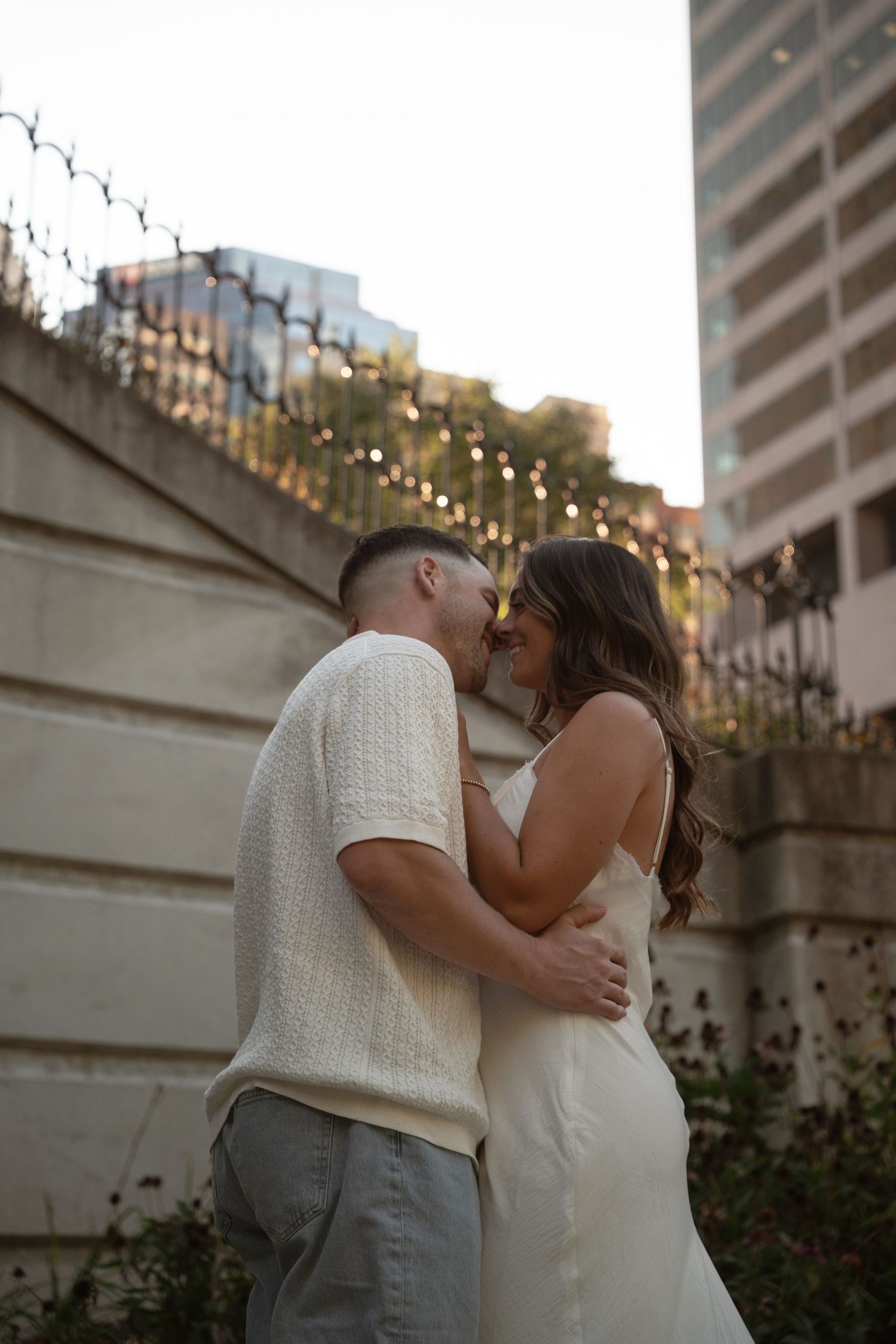 Romantic couple sharing an intimate moment against a wall with string lights in the background.