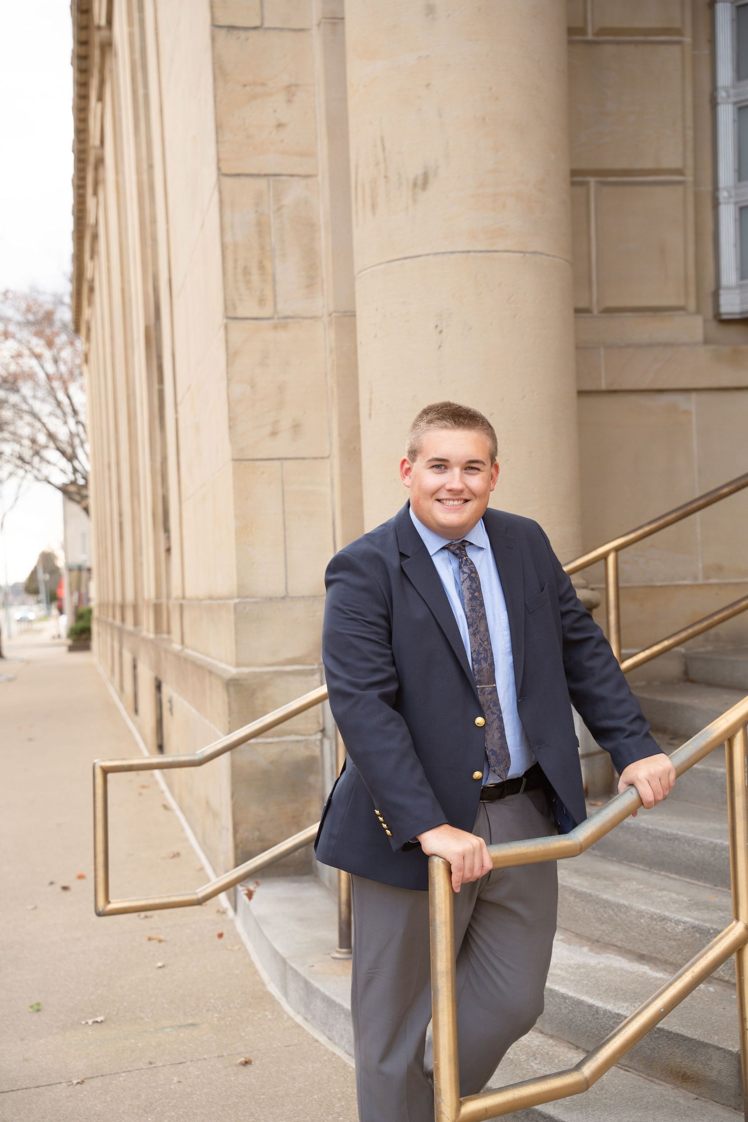 Senior professionally showcased in suit posed playfully on stone steps of classic building exterior.
