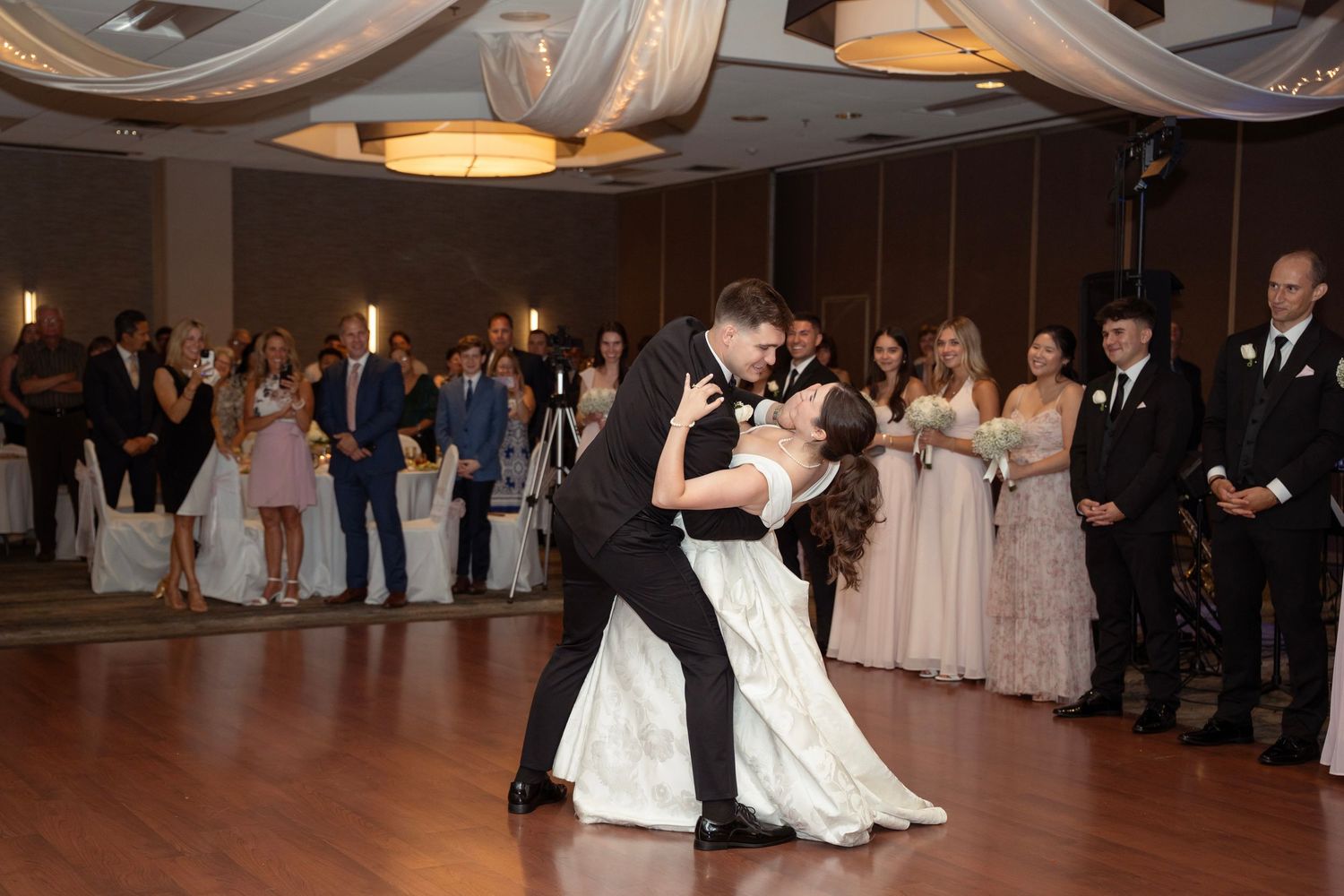 Wedding reception dance floor with guests celebrating in dimly lit ballroom during couples first dance