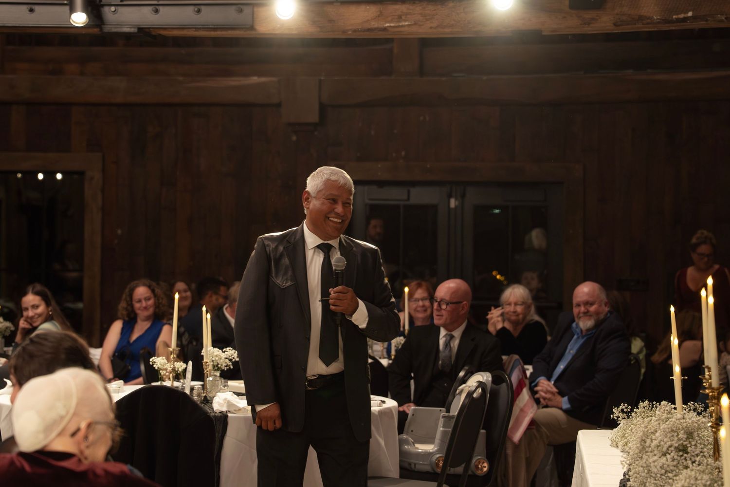 Father of Bride makes toast in front of wedding guests during an indoor reception celebration.