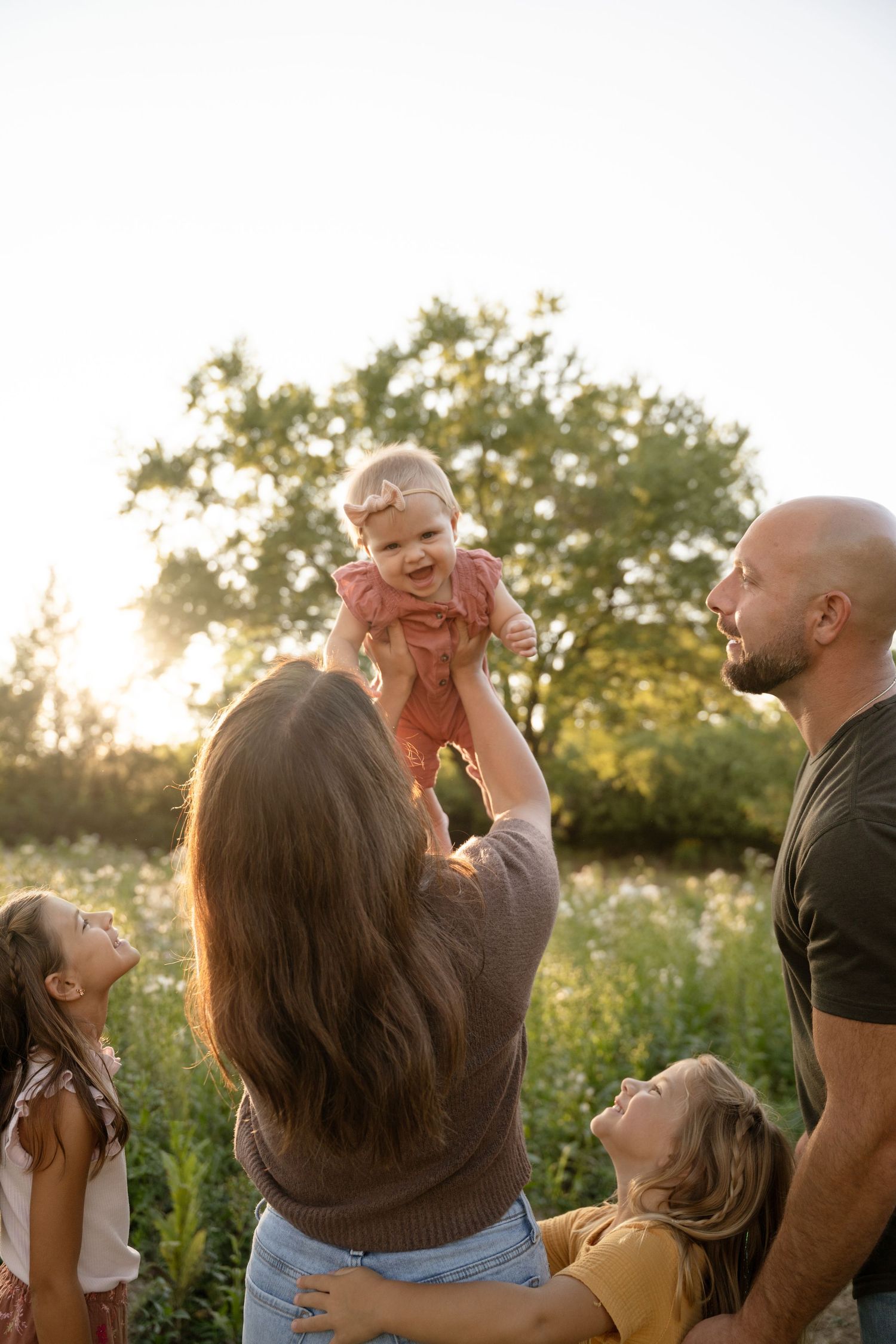 Family playing together in a sunlit meadow during golden hour session.