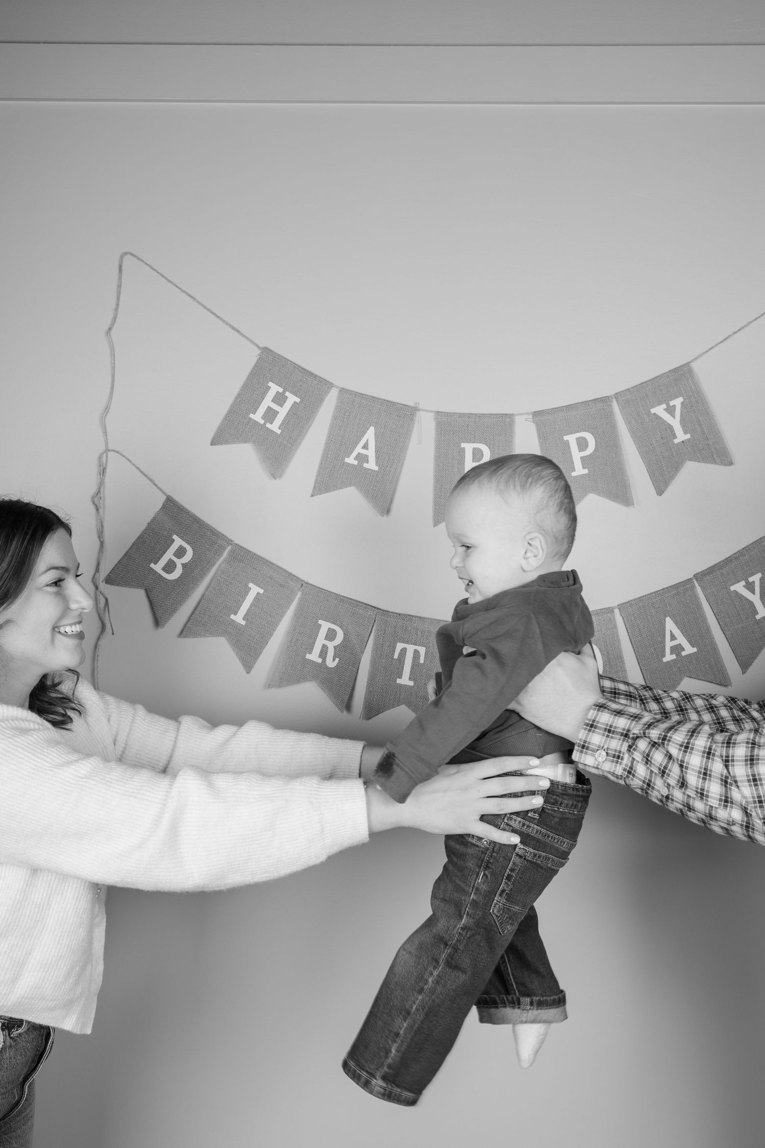 Black and white family photo in studio with happy birthday banner and playful poses.
