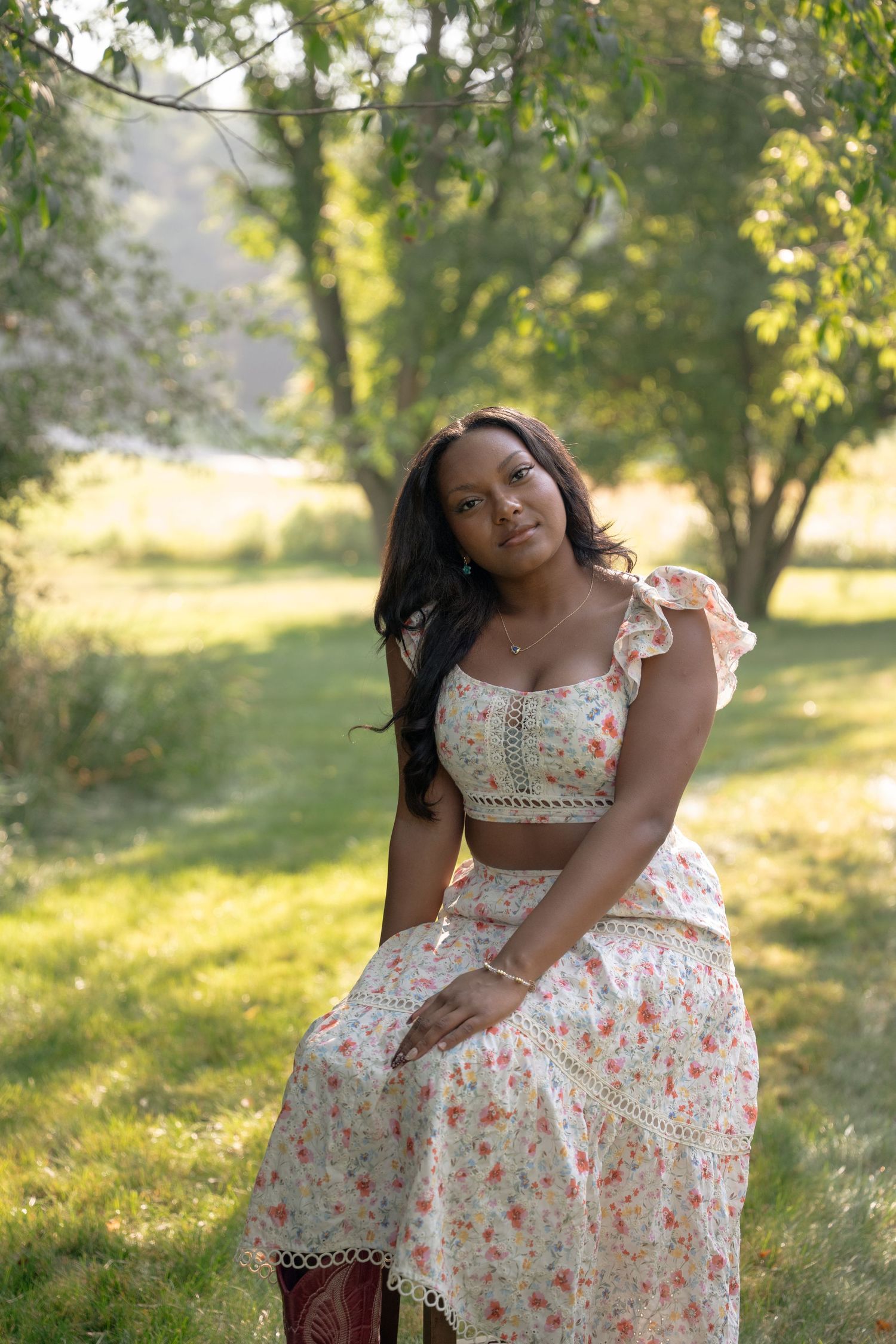 Floral summer dress captured in golden sunlit meadow during outdoor senior photo session.