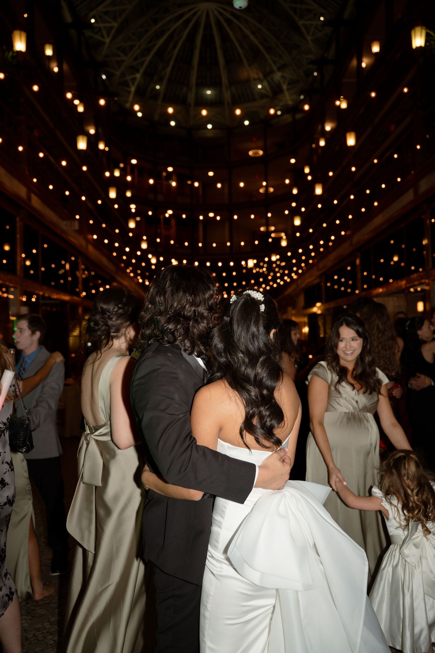 Wedding reception dance floor filled with guests under twinkling string lights in a rustic venue.