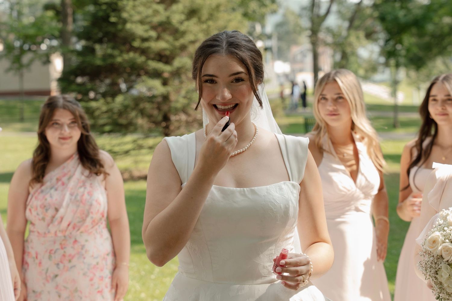 Bridesmaids in floral pink dresses gather outdoors for photos.