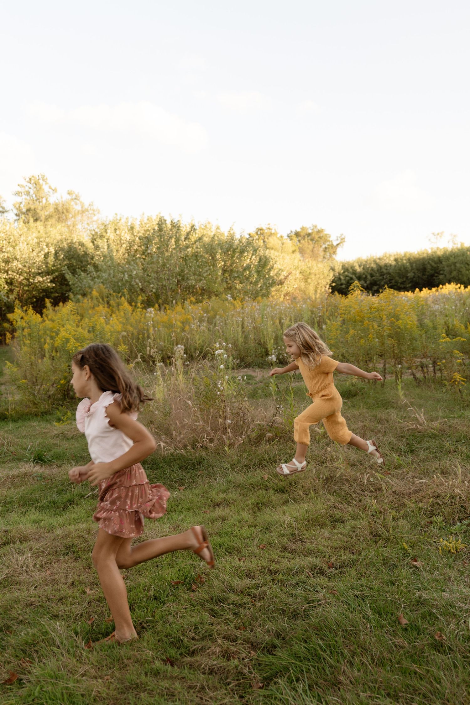 Children playing and running through a grassy field during  a sunset family session.