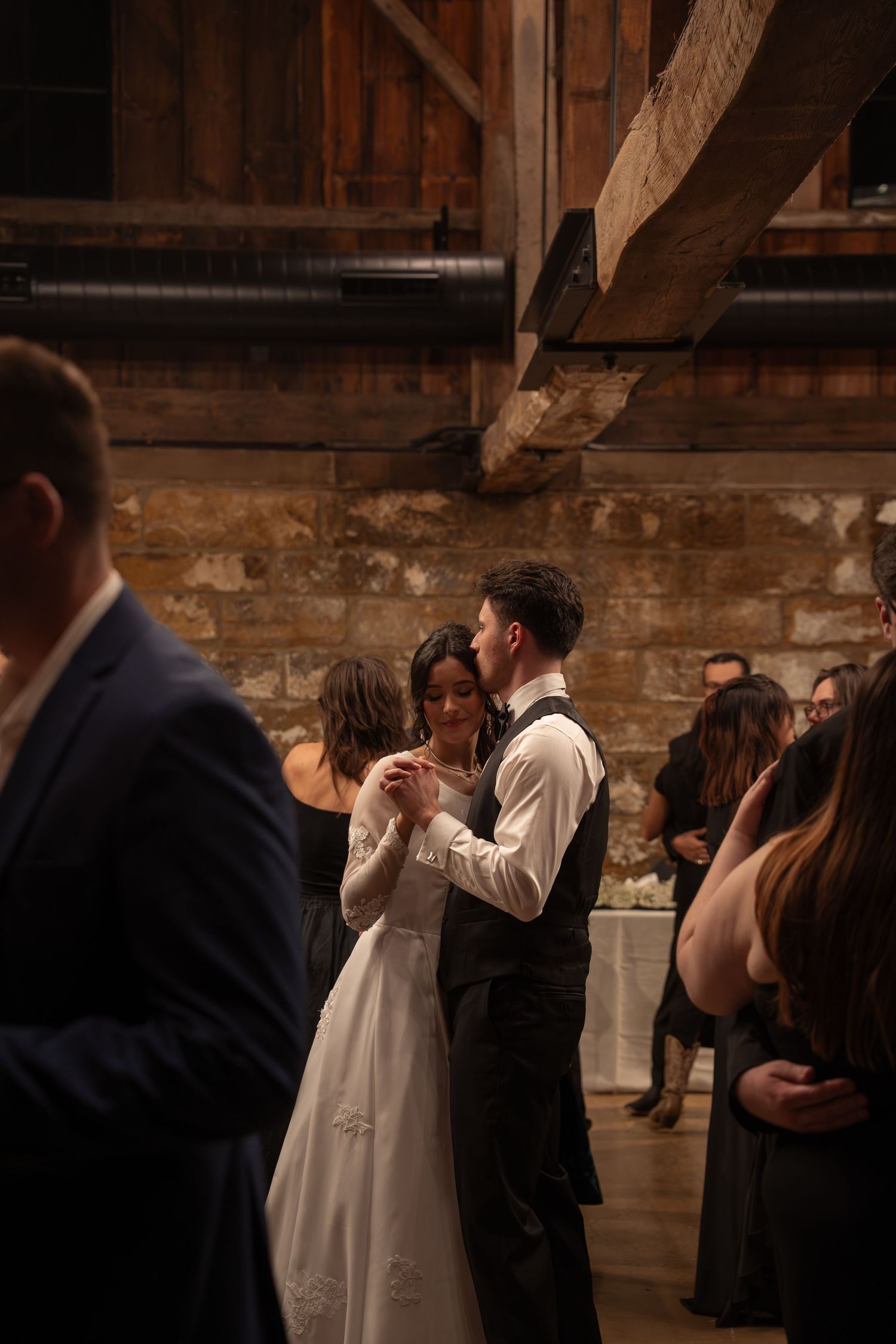Wedding guests dance while framing the bride and groom celebrate in a rustic barn venue.