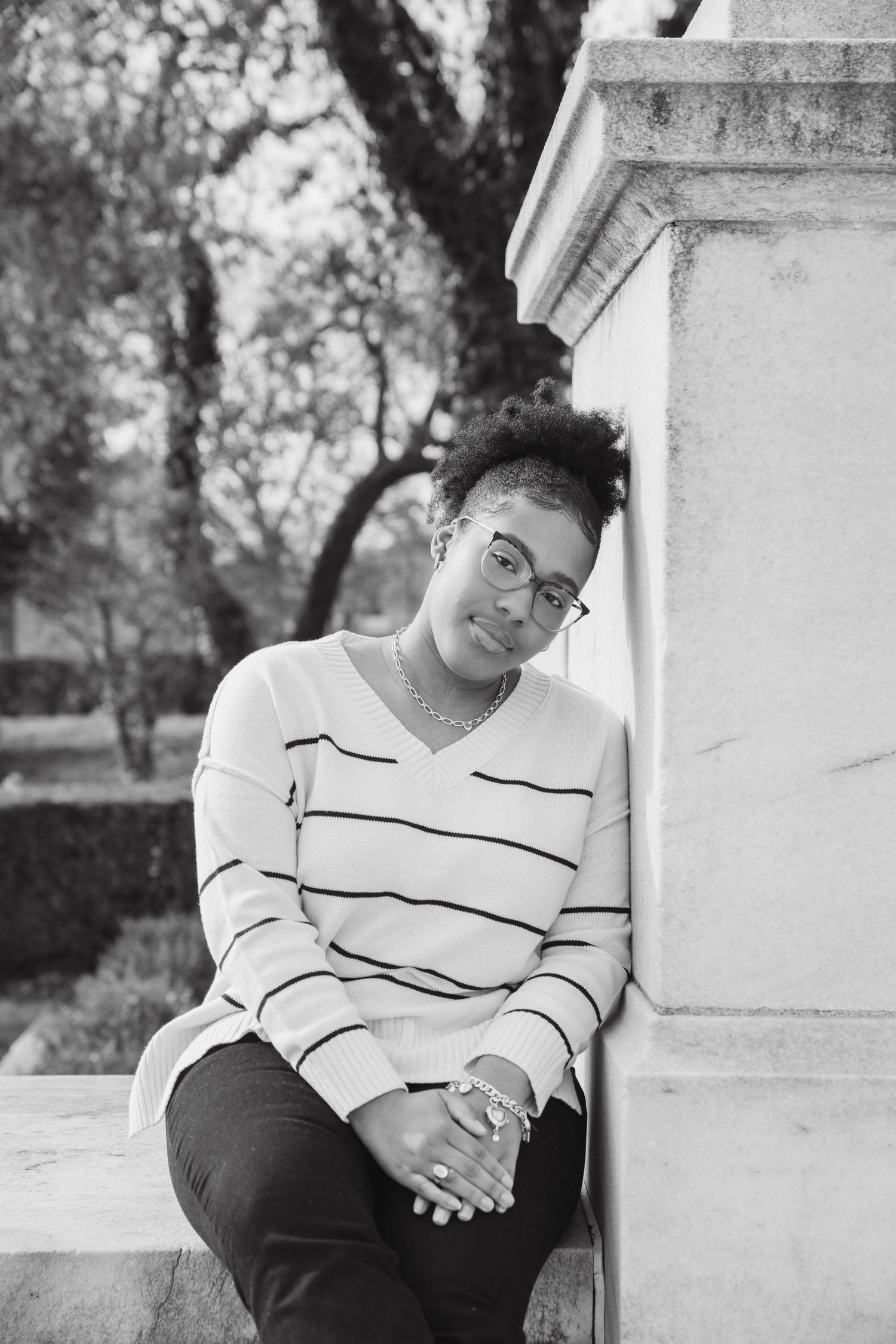 Black and white senior portrait session featuring casual striped sweater against white architectural backdrop.