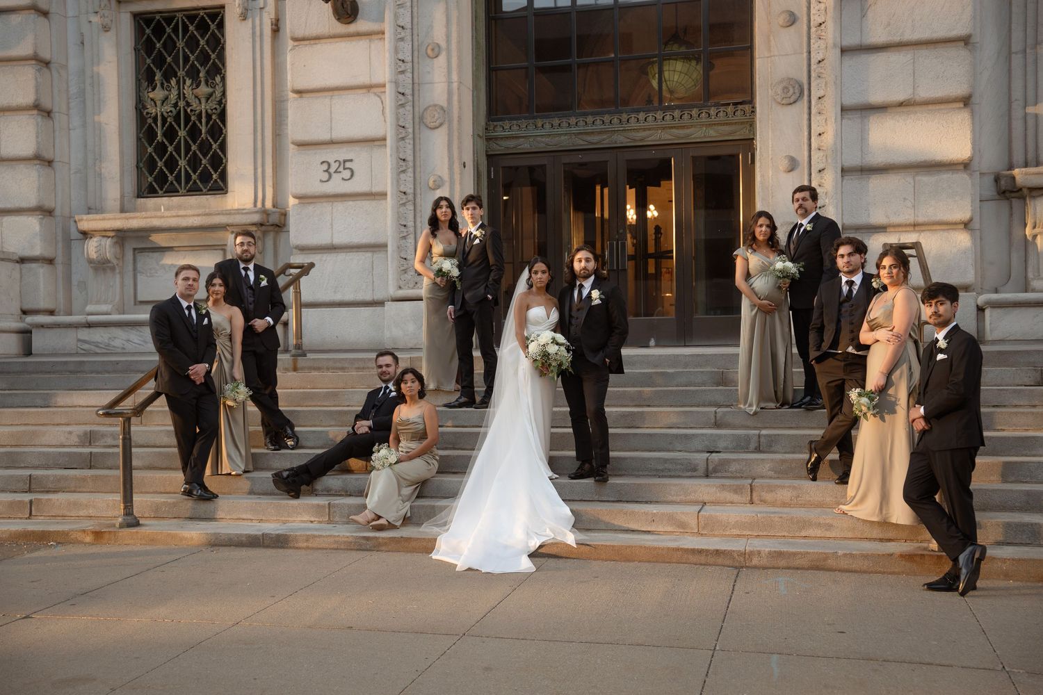 Wedding photographers capture the newlyweds and bridal party on elegant stone steps of a historic building at sunset.