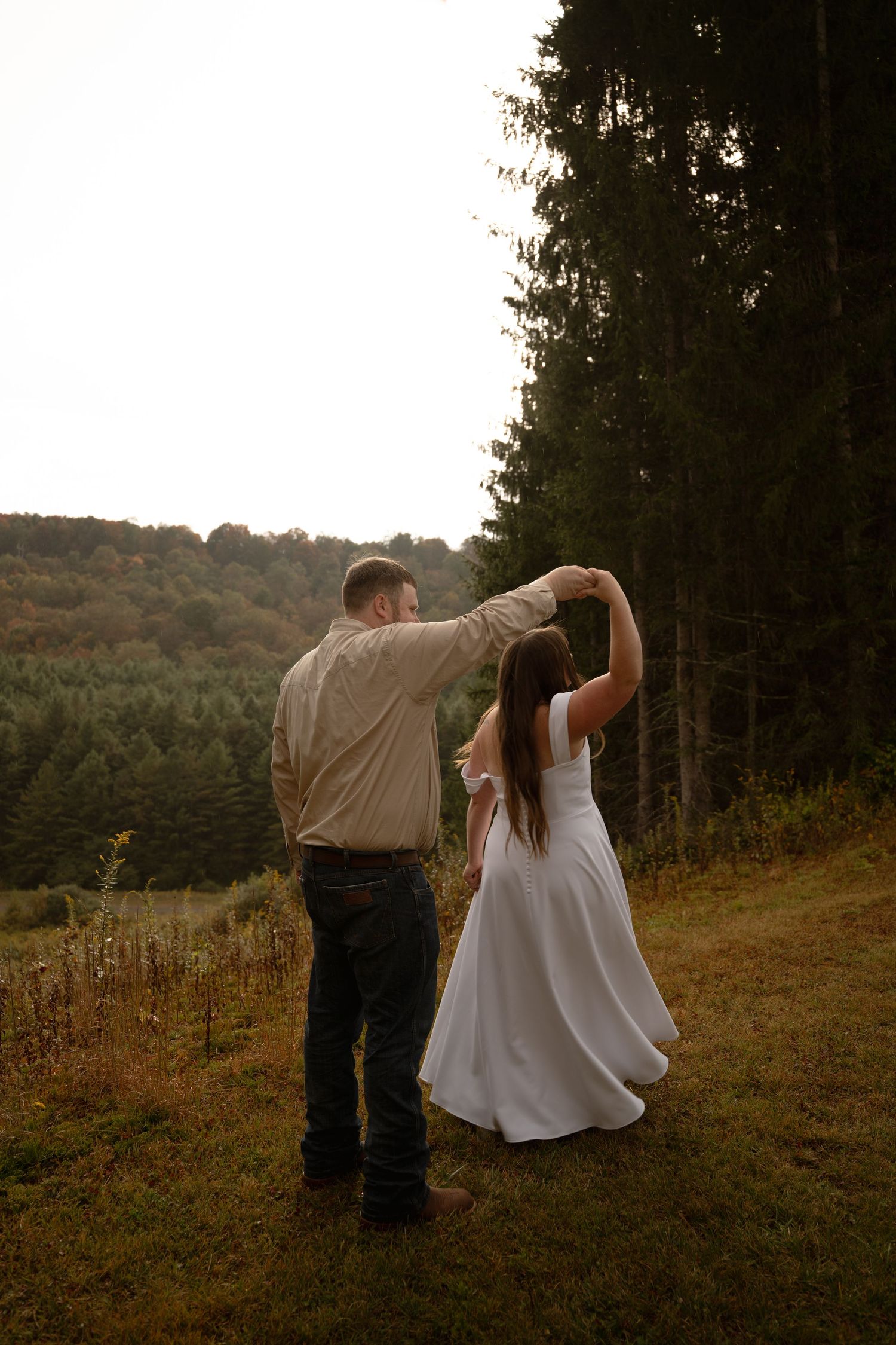 Silhouetted wedding couple dances at sunset against rural West Virginia valley backdrop.