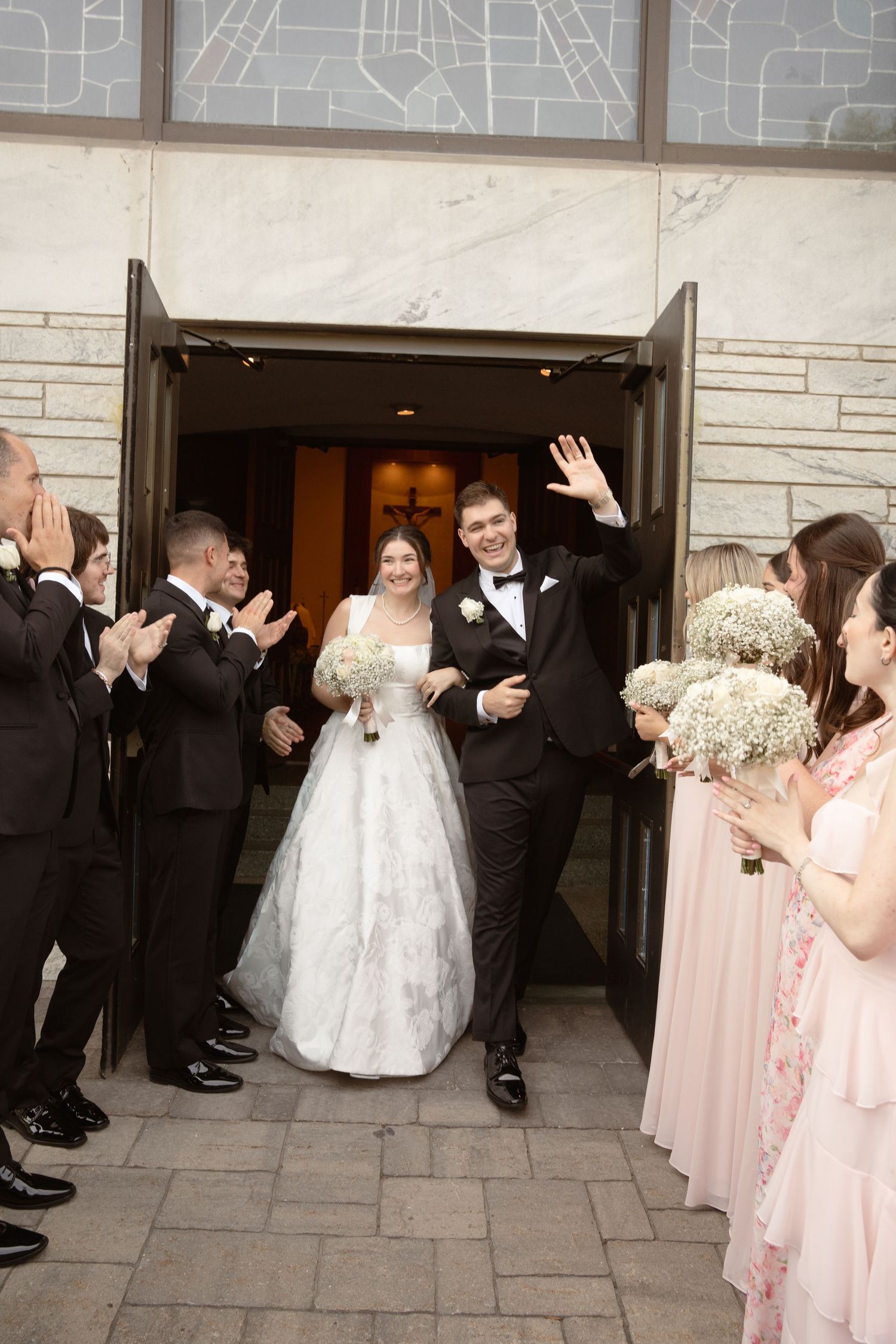 Wedding party exits New York church building with bride in white gown and bridesmaids in pink dresses.