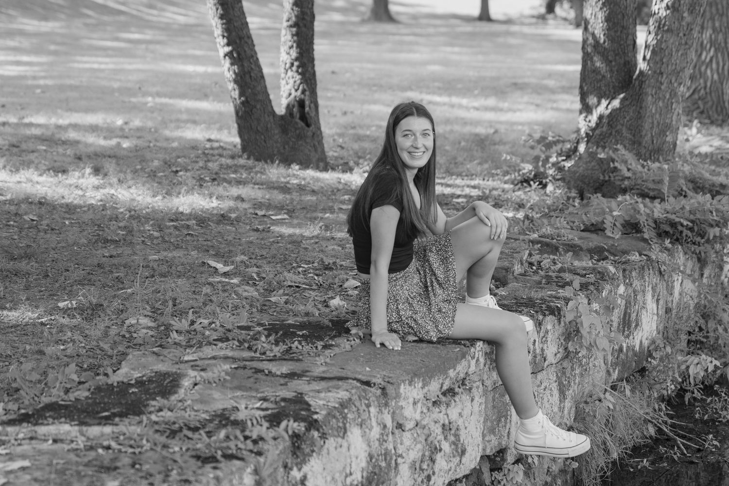 A black and white photo shows a senior sitting on grass in a natural outdoor park setting.